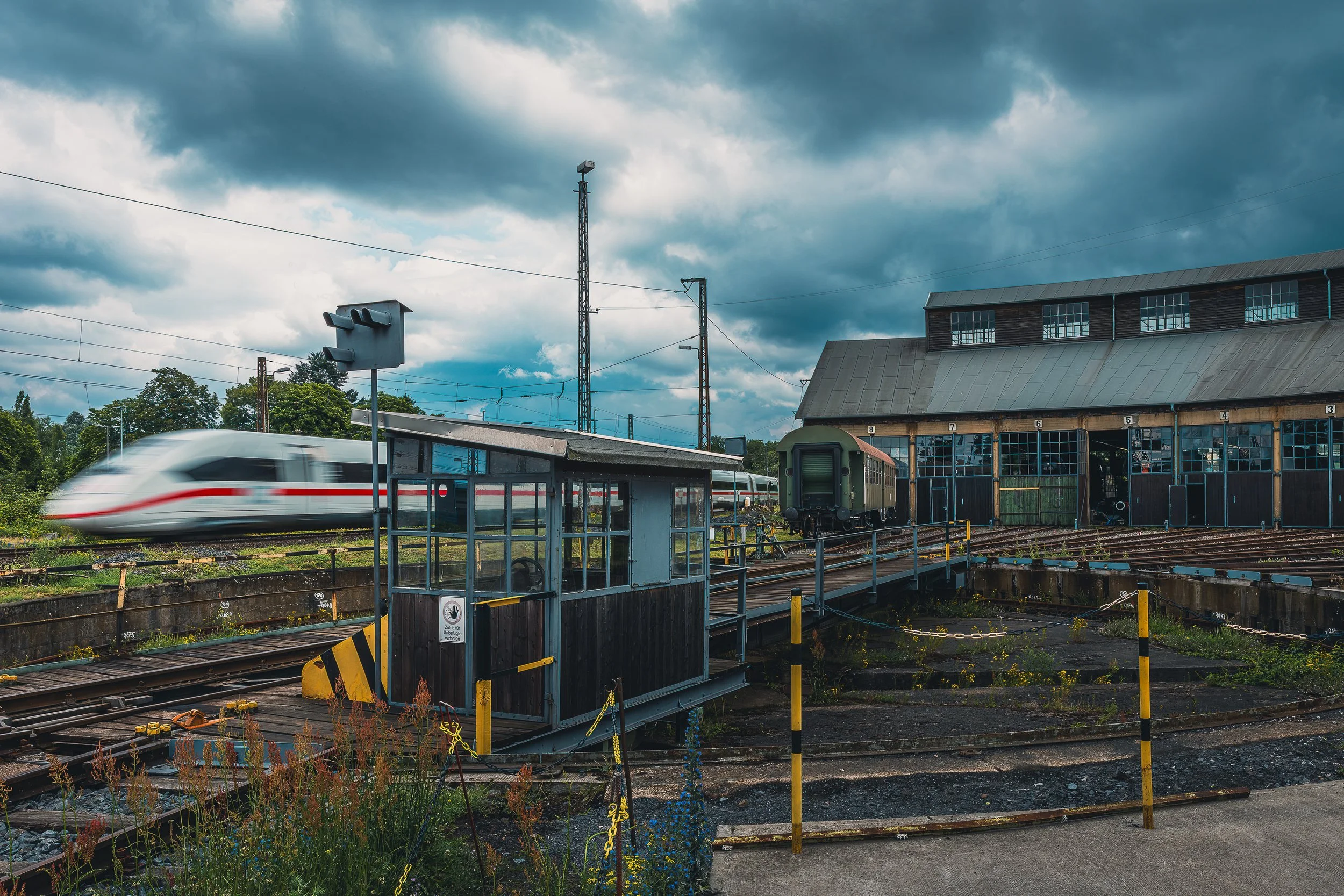 ICE train passing the historic locomotive shed and turntable in Hanau beneath dramatic clouds