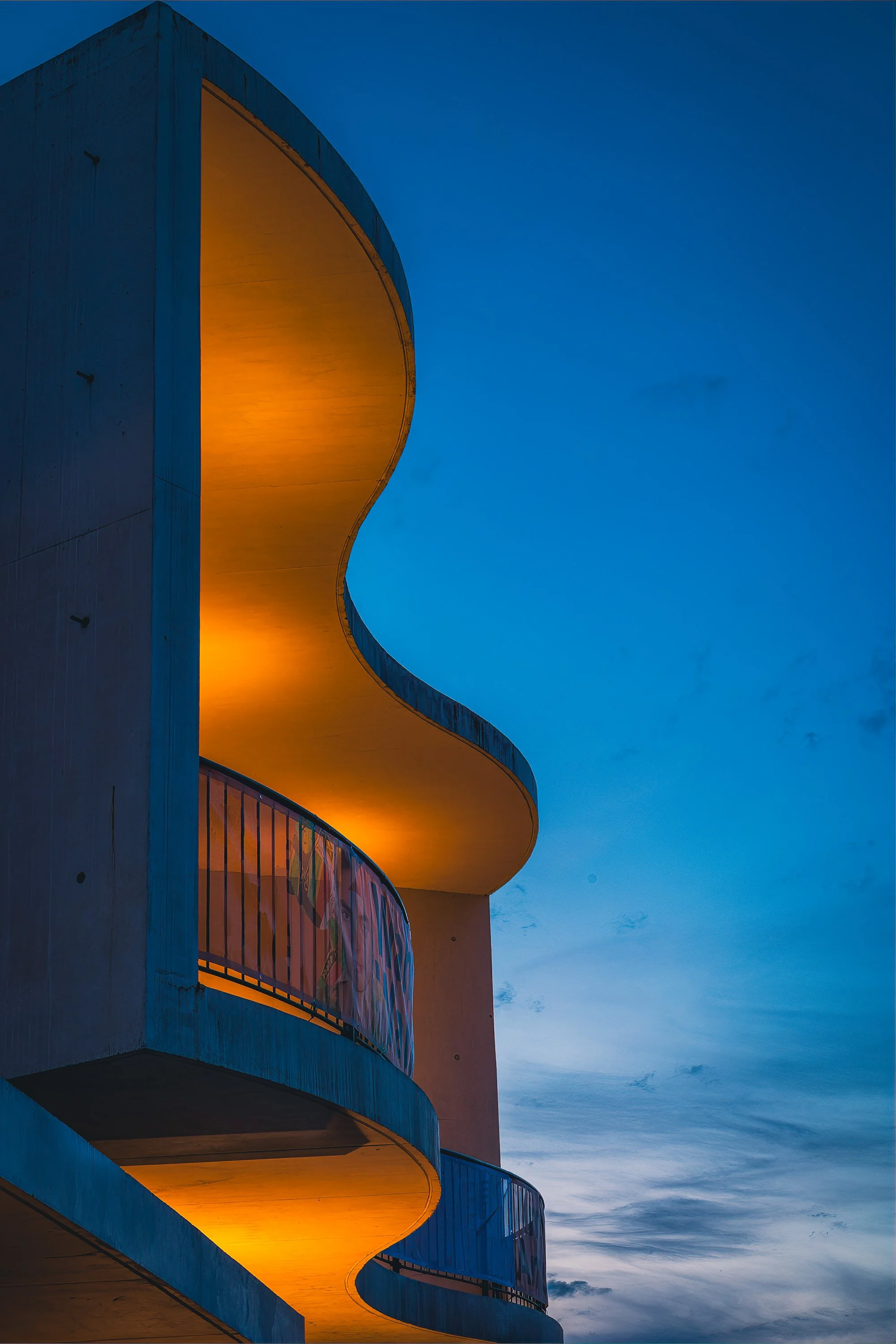 Curved concrete architecture of Staatstheater Darmstadt illuminated with warm light against a blue evening sky