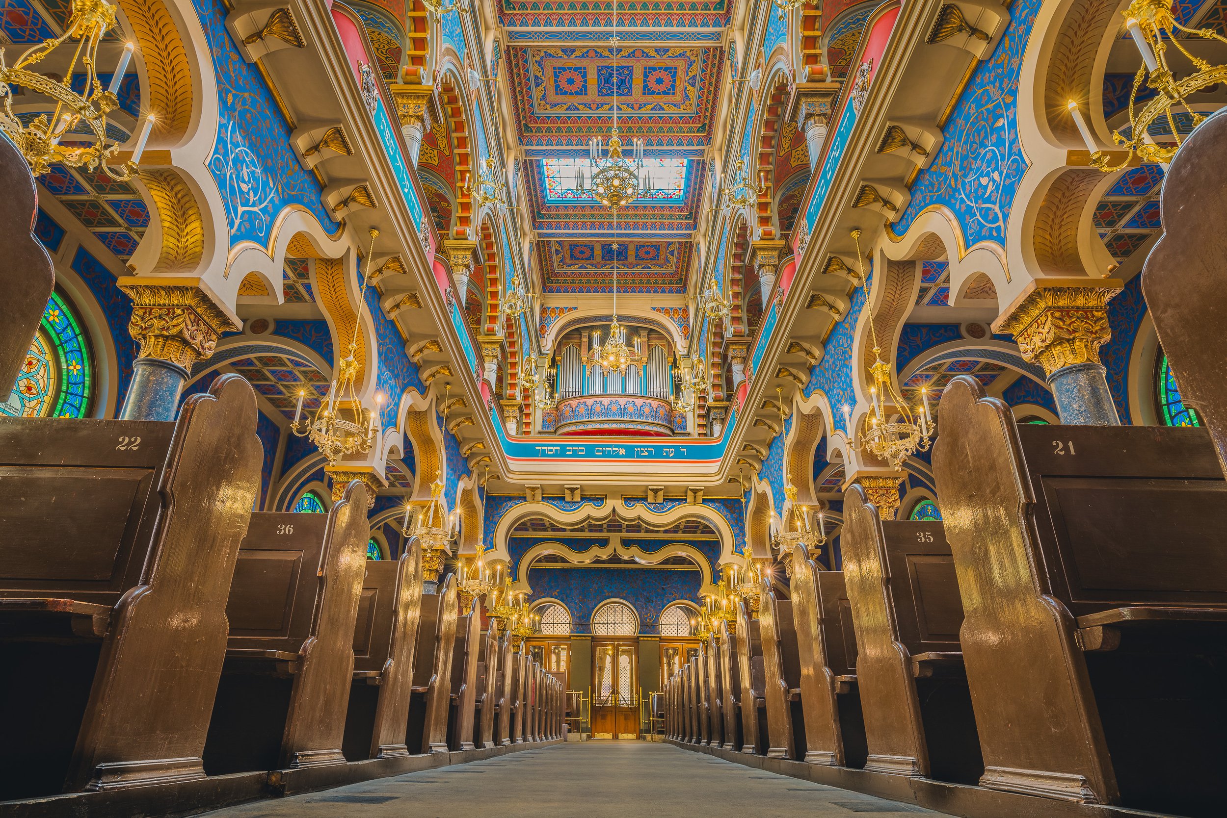 Ornate interior of Jerusalem Synagogue in Prague with richly colored arches and rows of wooden pews