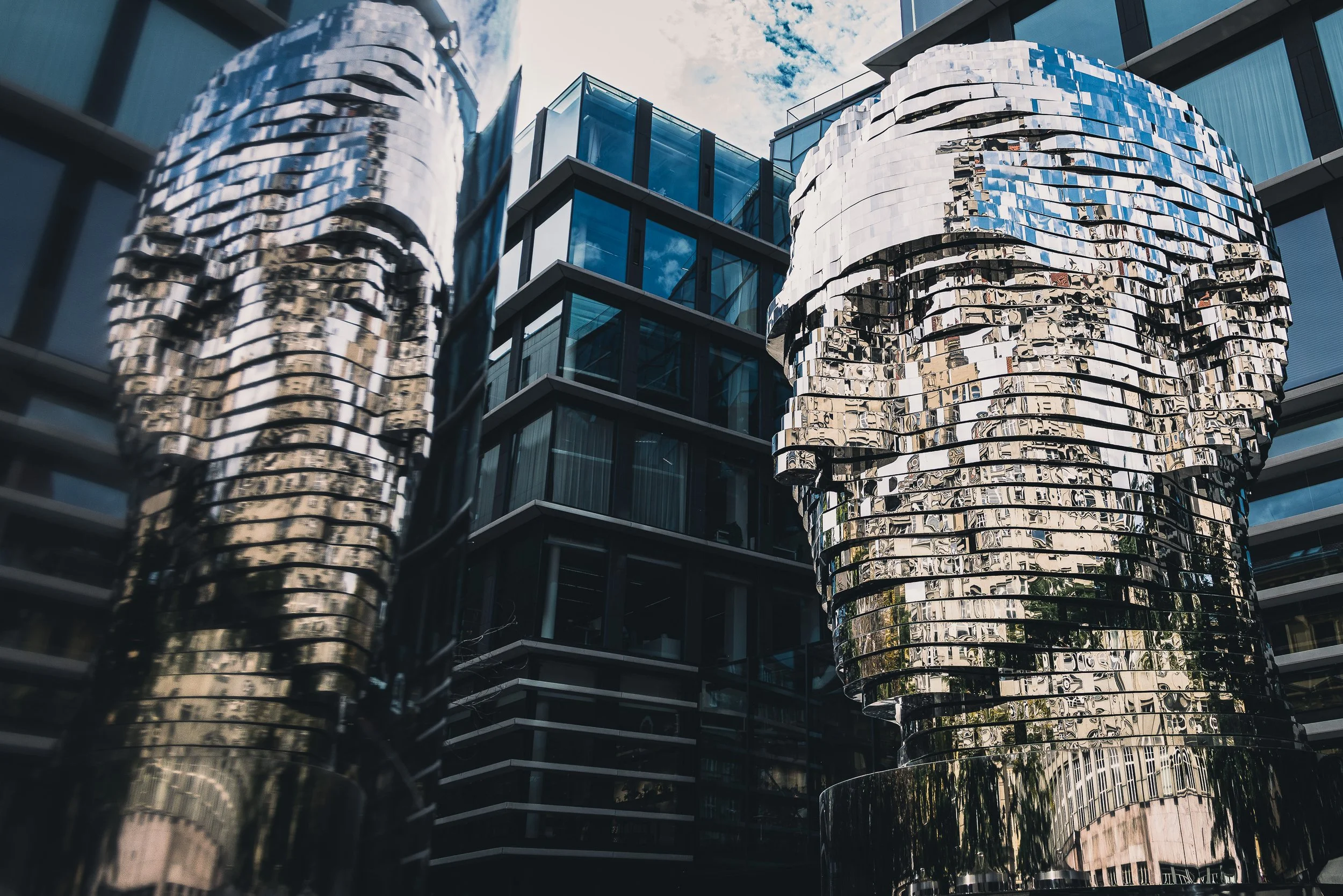 Mirrored rotating head sculpture of Franz Kafka reflected in a glass facade in Prague