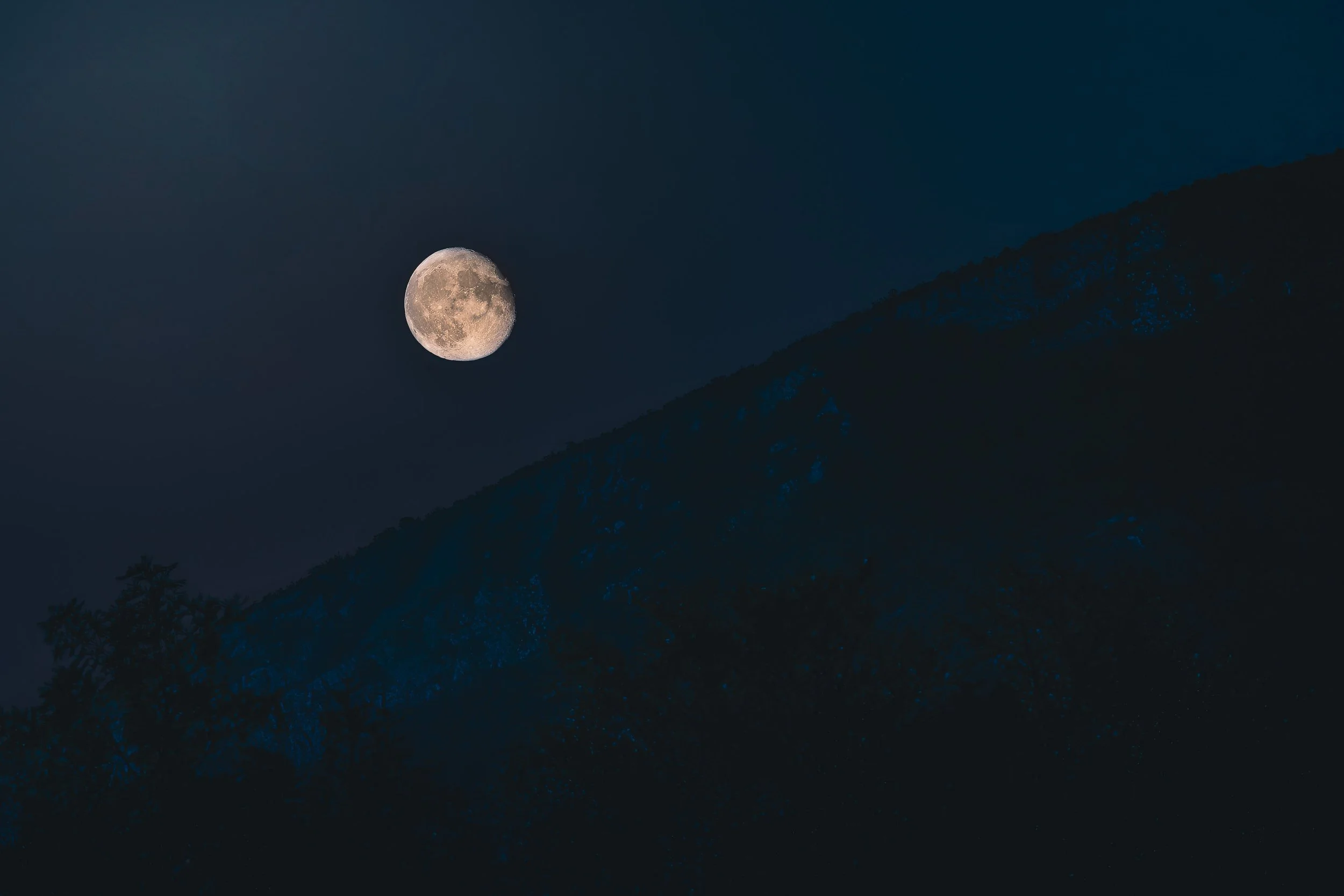 Small moon above a dark mountain ridge with large areas of empty sky