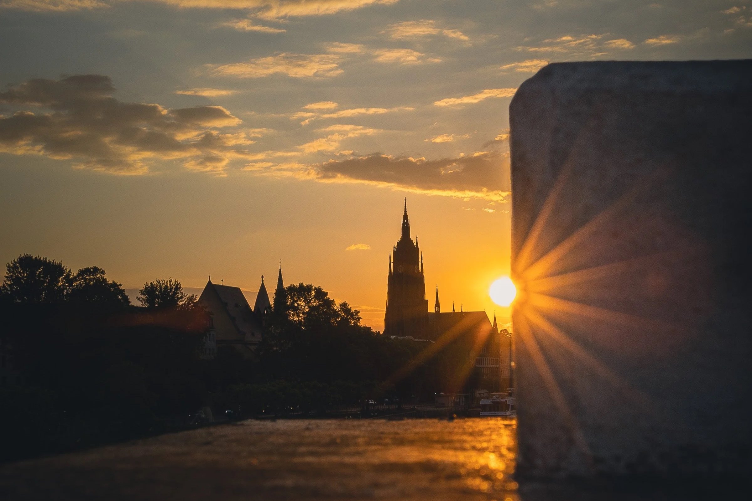 Frankfurt Cathedral silhouetted at sunset with the sun breaking past a bridge pier