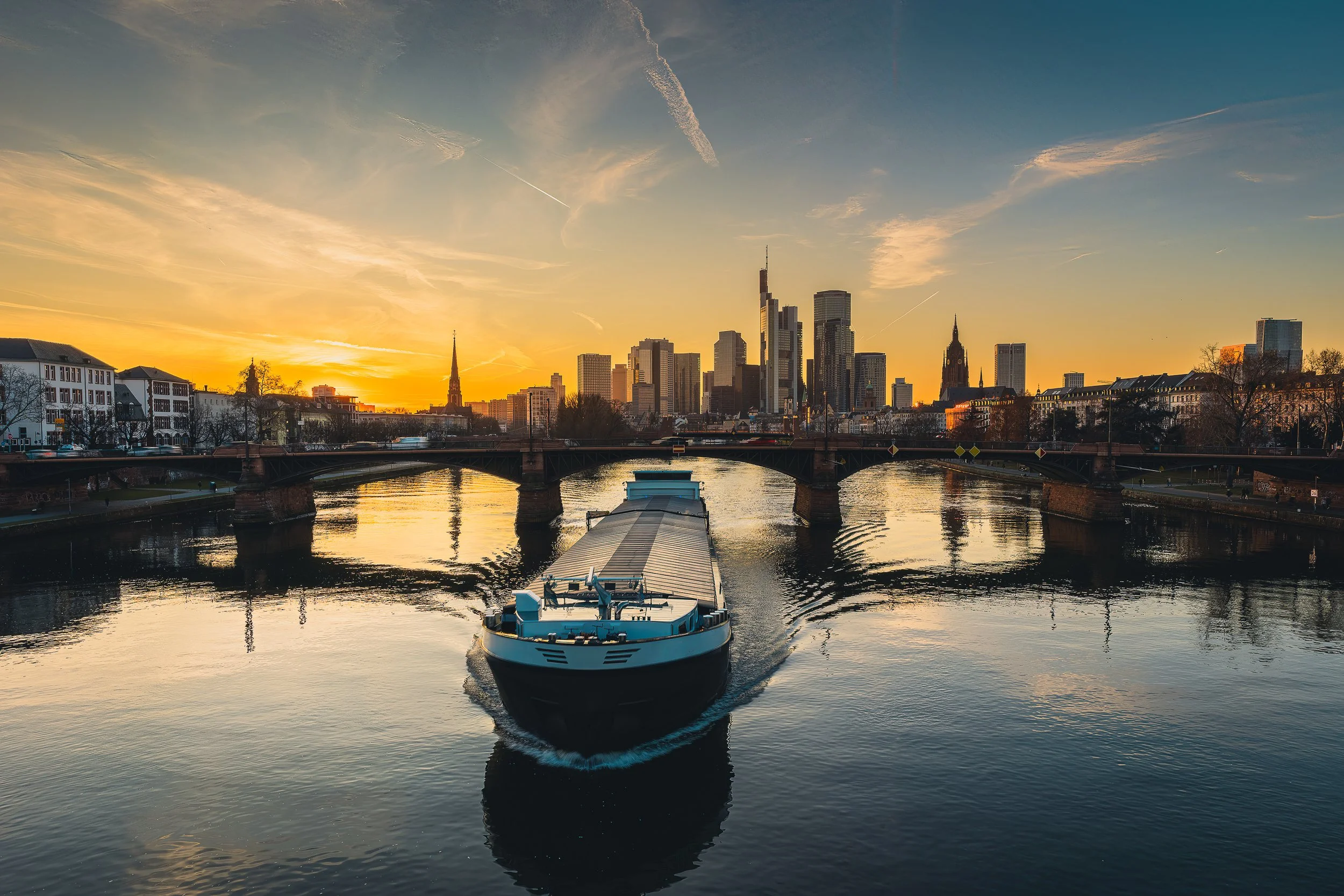 Frankfurt skyline at sunrise with a boat reflected in the Main River.