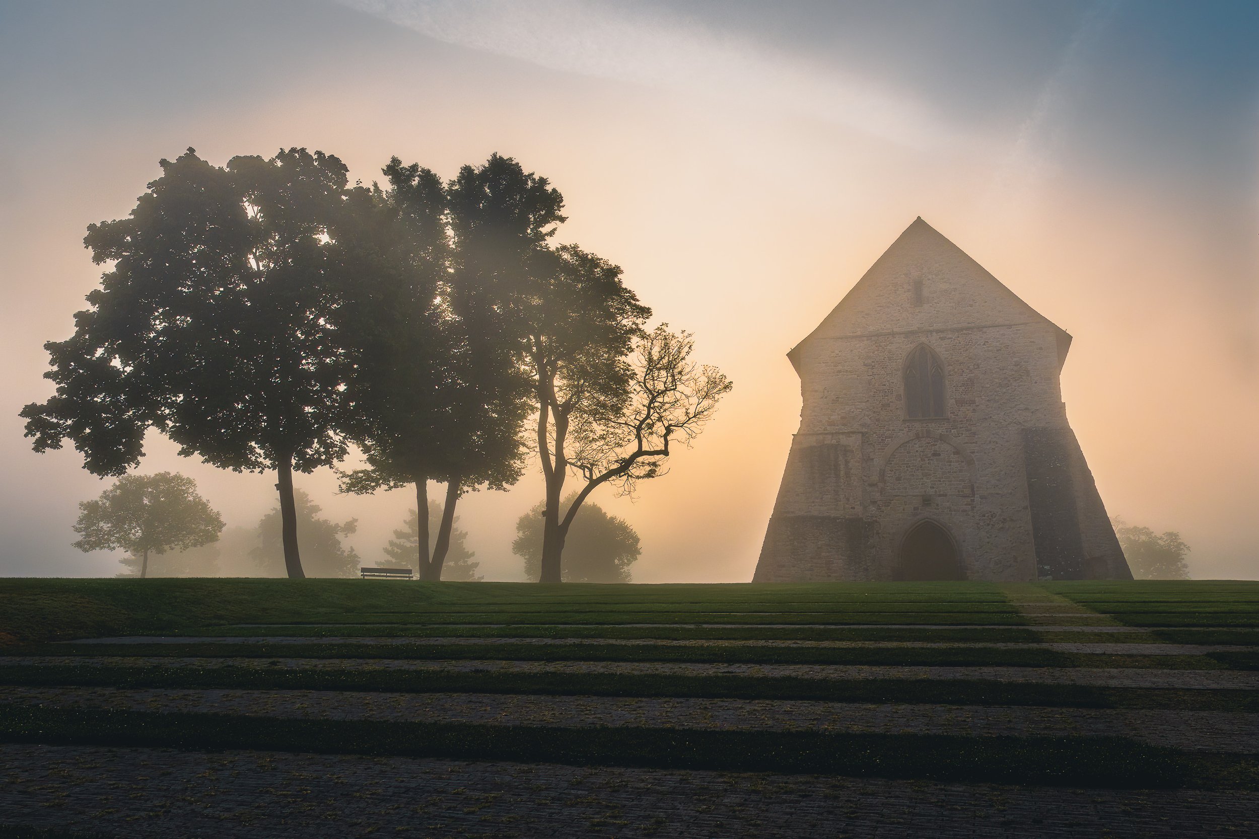 Historic monastery building and trees emerging from soft morning fog at Lorsch Abbey