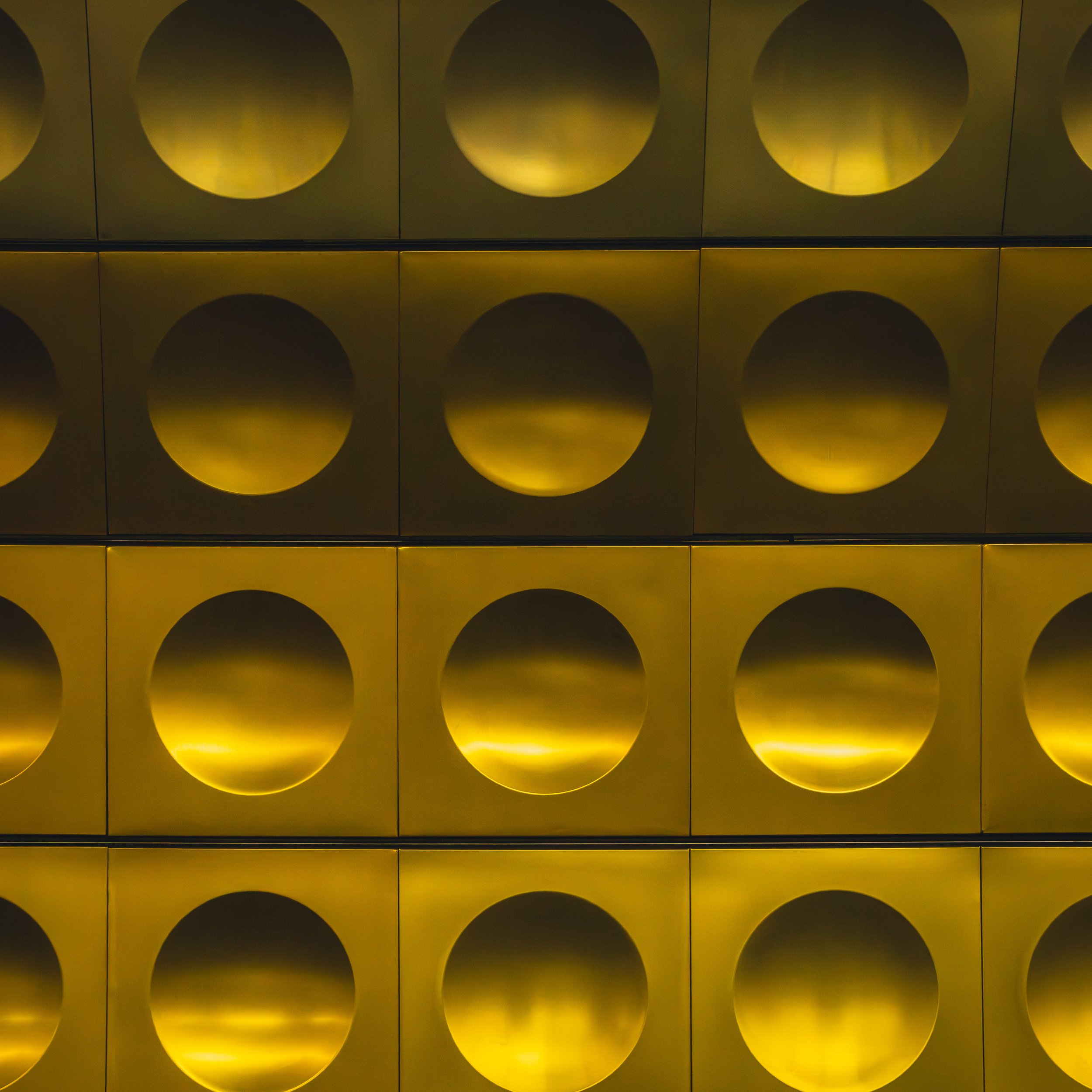 Repeating yellow wall panels with circular recesses at Můstek metro station in Prague