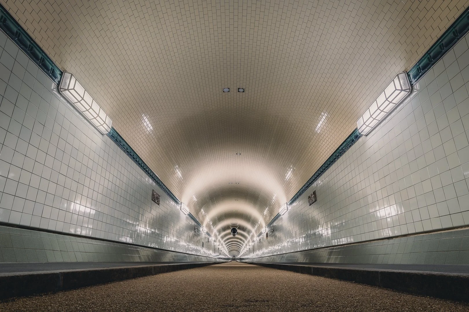 Symmetrical tunnel interior in Hamburg with tiled walls, repeating ceiling lights and a strong central vanishing point.