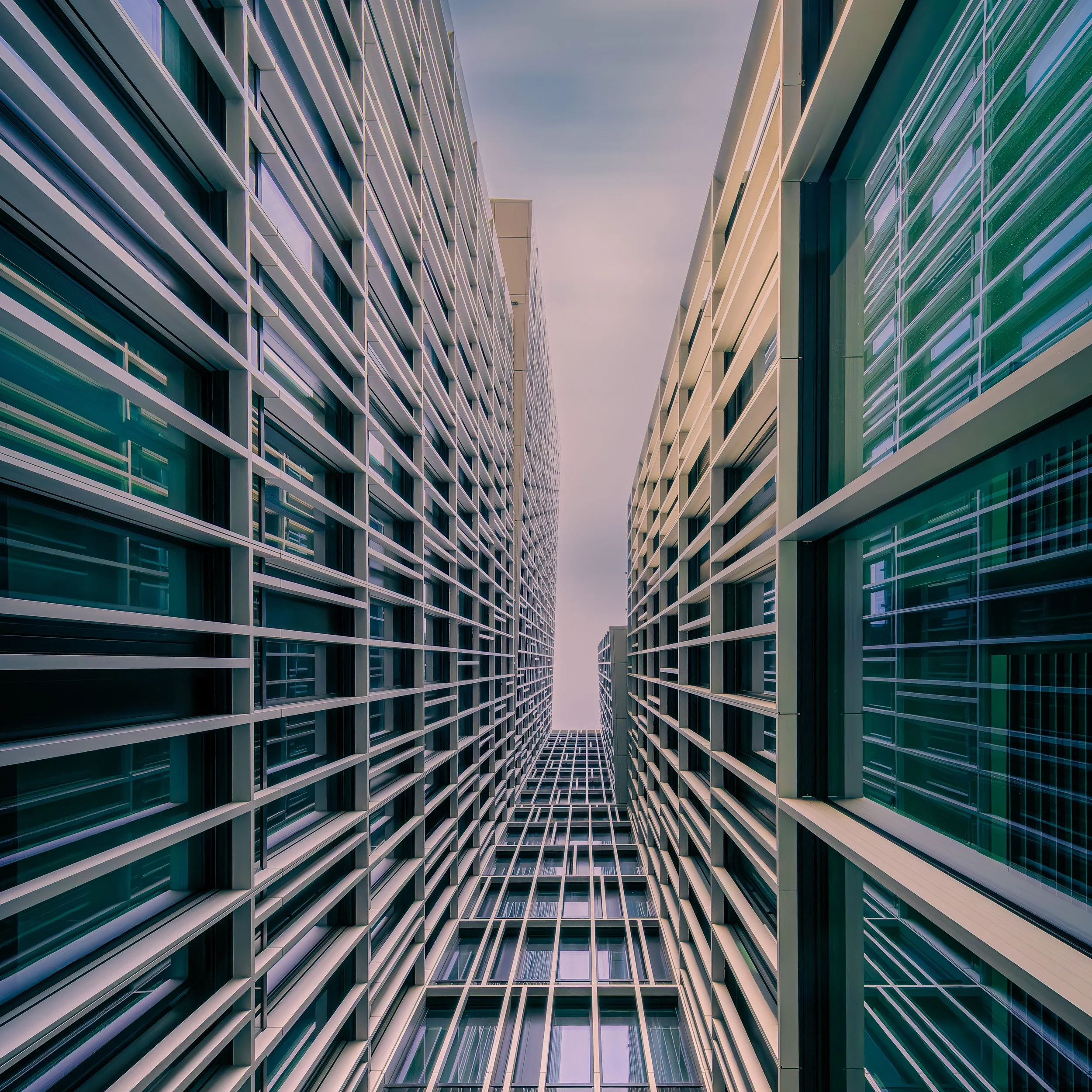 Narrow view between modern facades with repeating horizontal lines converging toward the sky