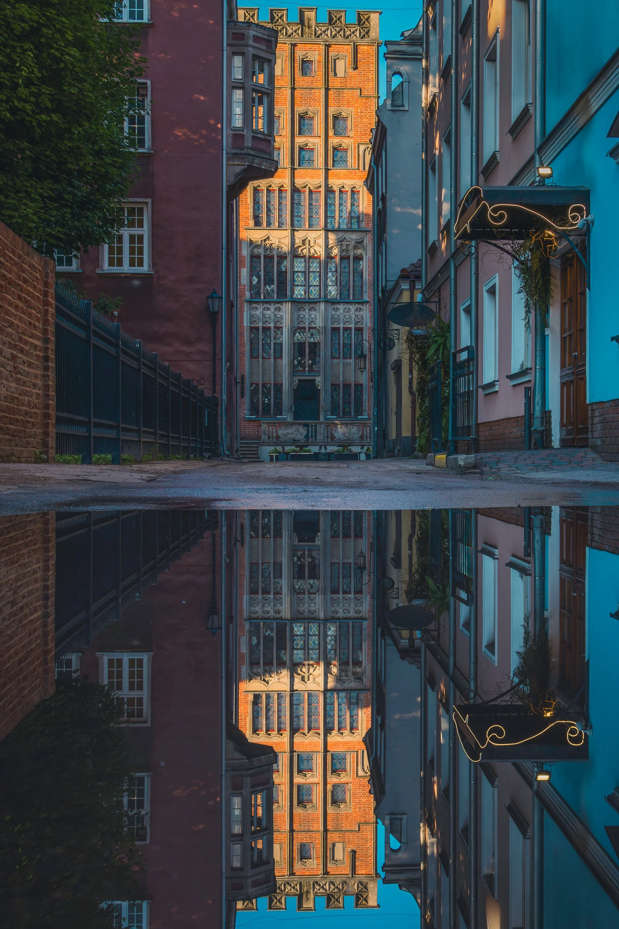 Narrow Gdańsk street with an ornate brick facade reflected in a puddle