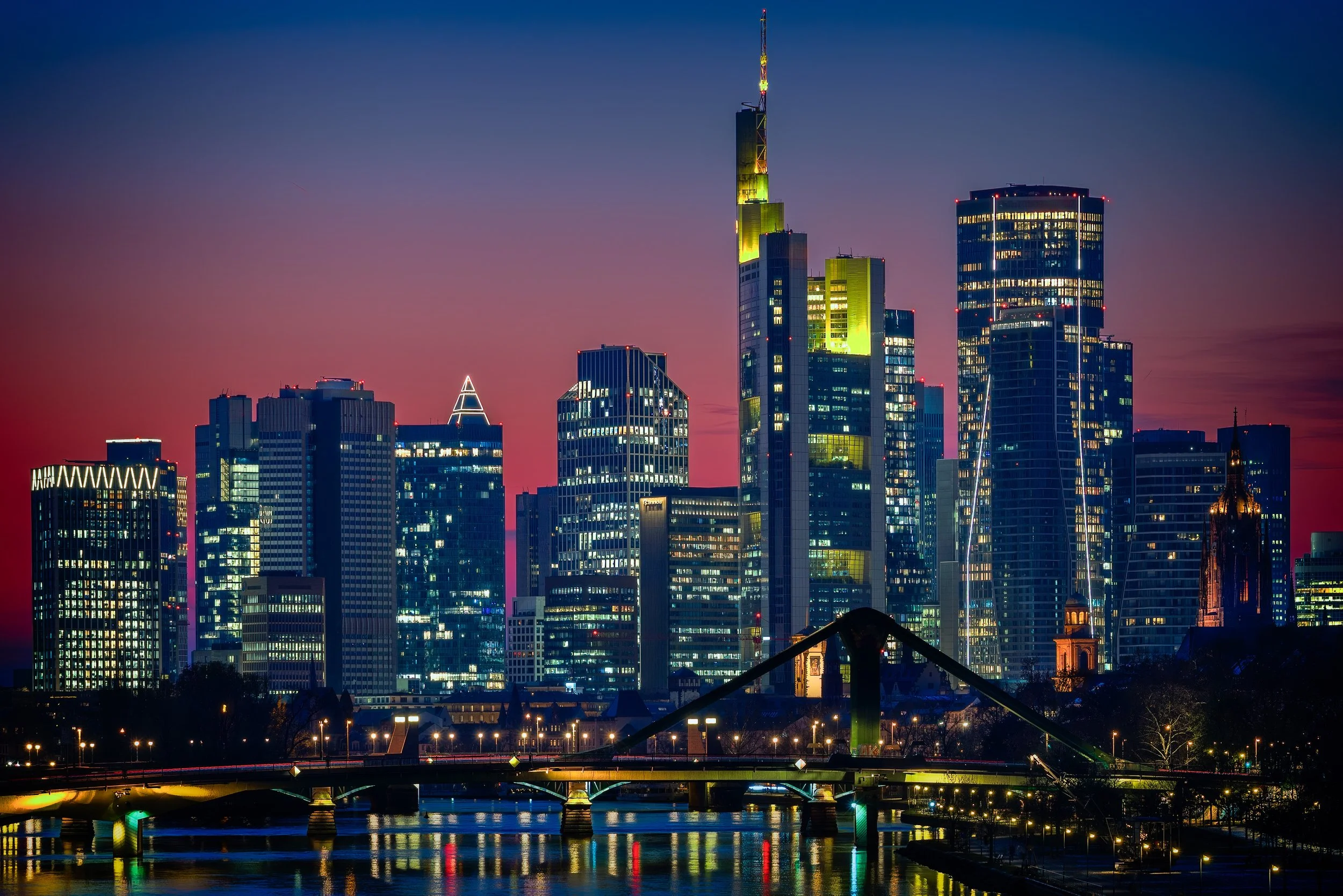 Frankfurt skyline illuminated at blue hour with Deutschherrn Bridge and reflections in the Main River