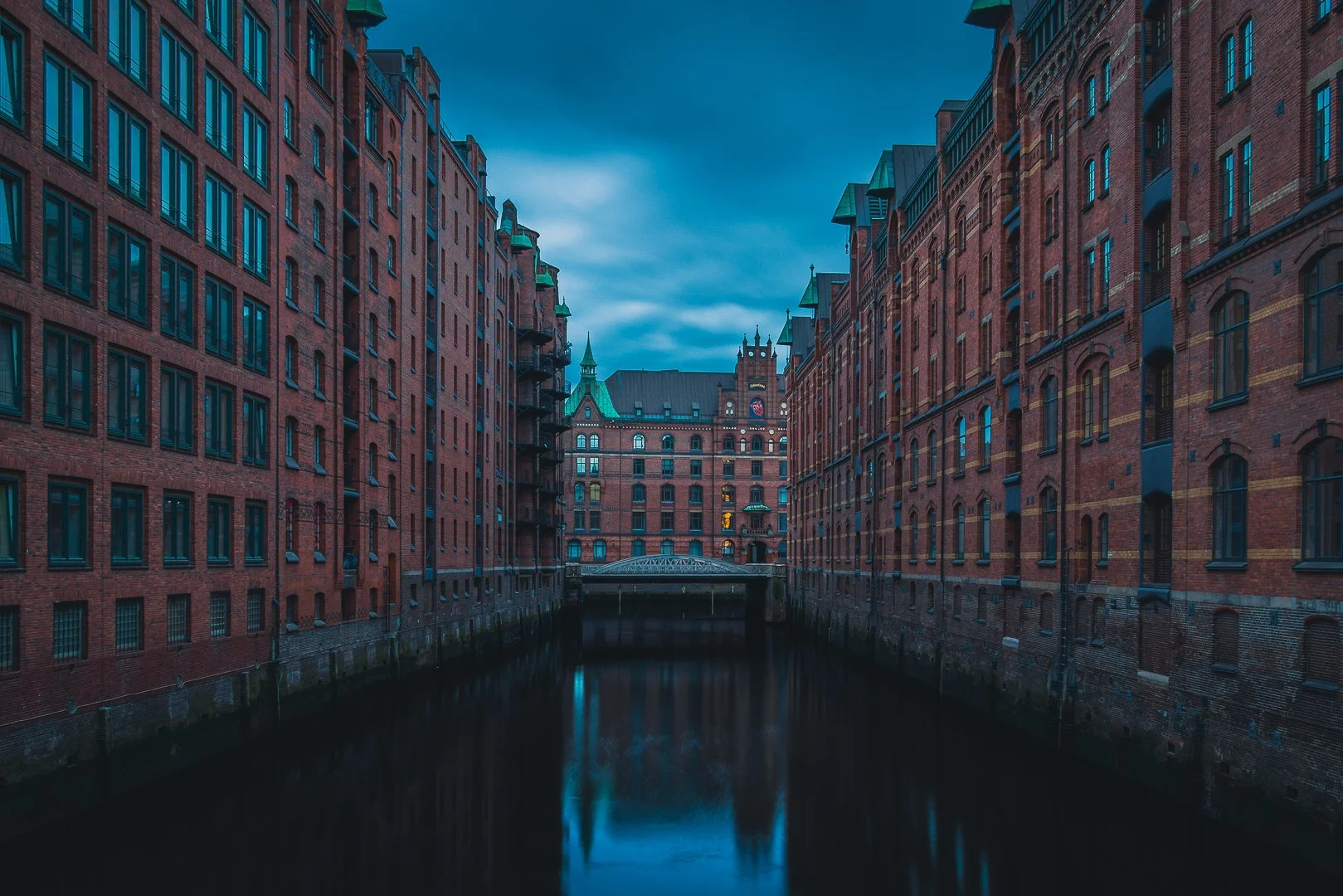 Quiet canal view in Hamburg’s Speicherstadt framed by symmetrical brick warehouses under a soft blue-grey sky.