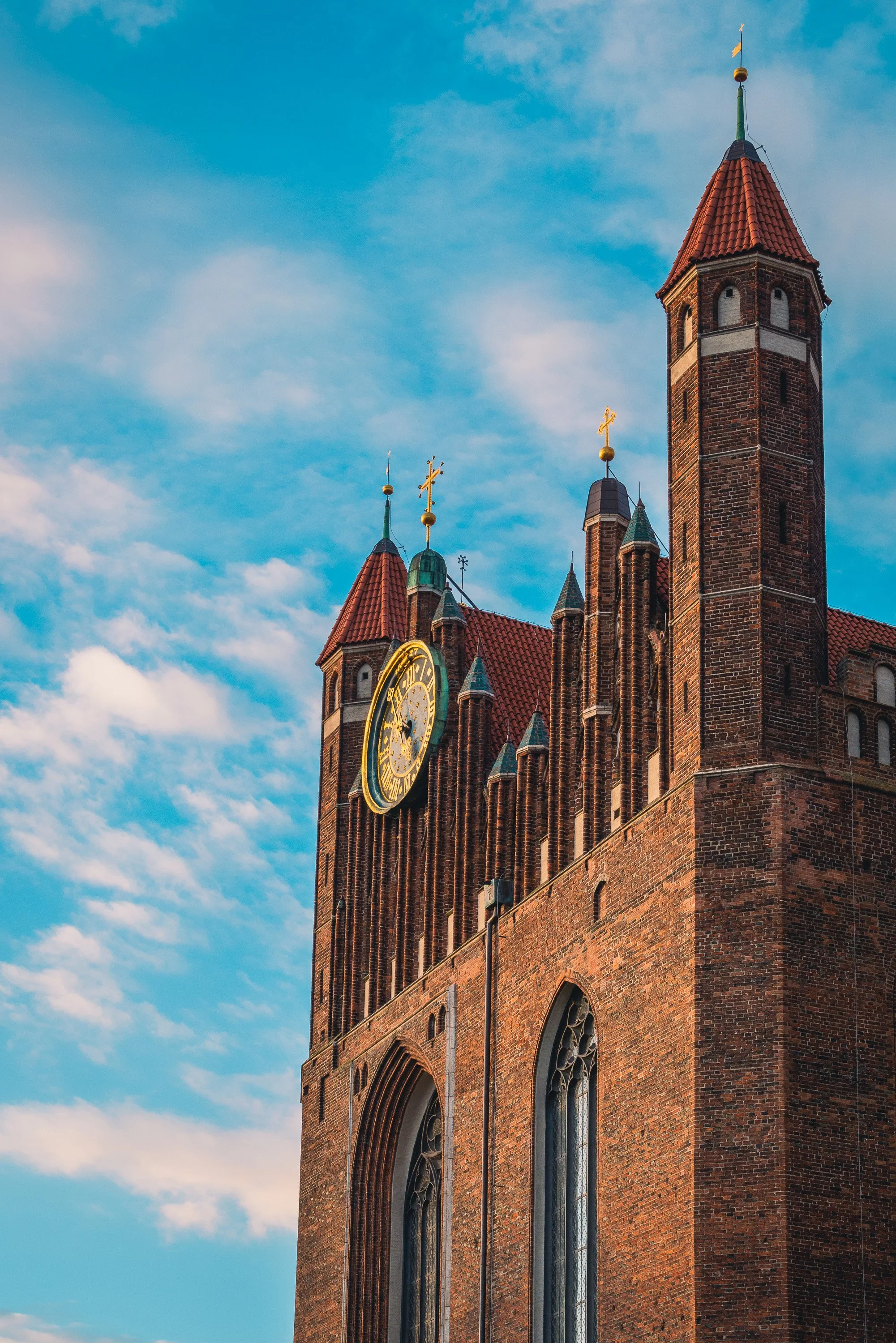 Brick church facade and clock tower rising against a blue sky in Gdańsk