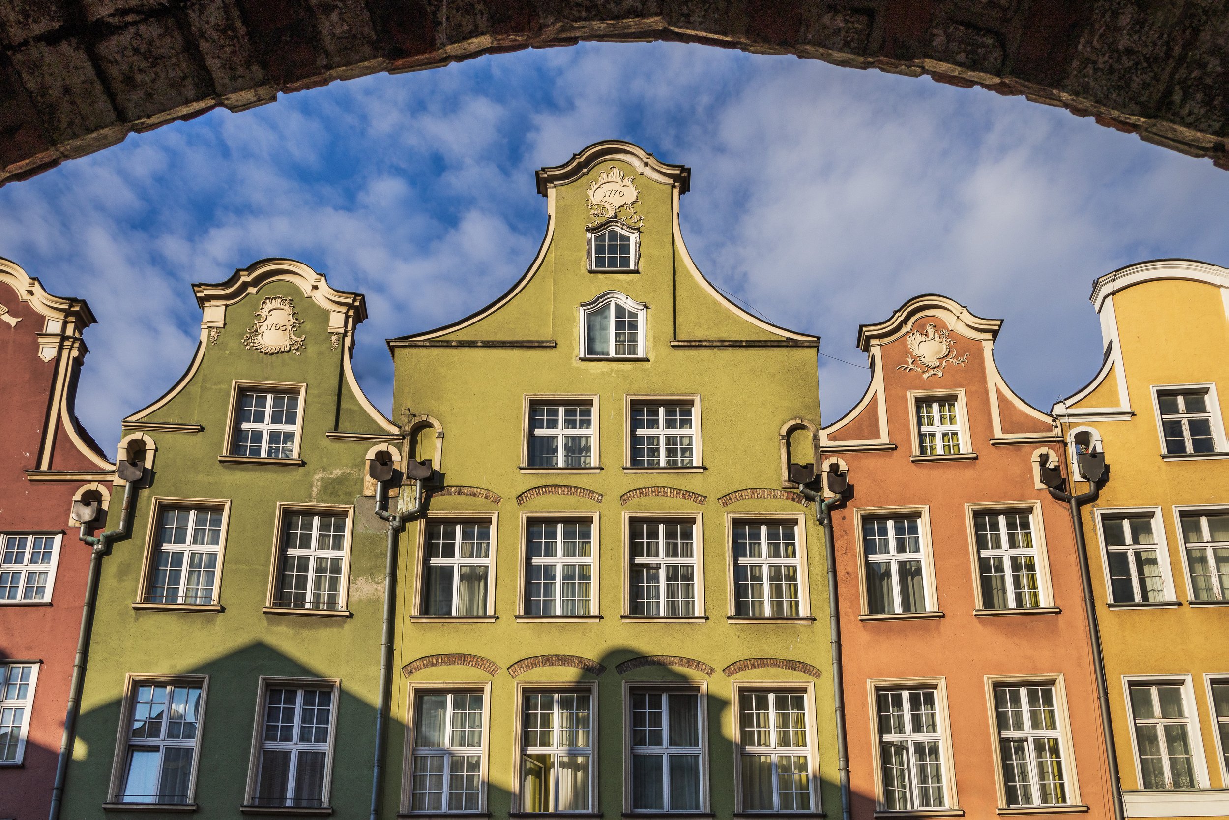 Historic buildings in Gdańsk viewed through an arched passage in the early morning.