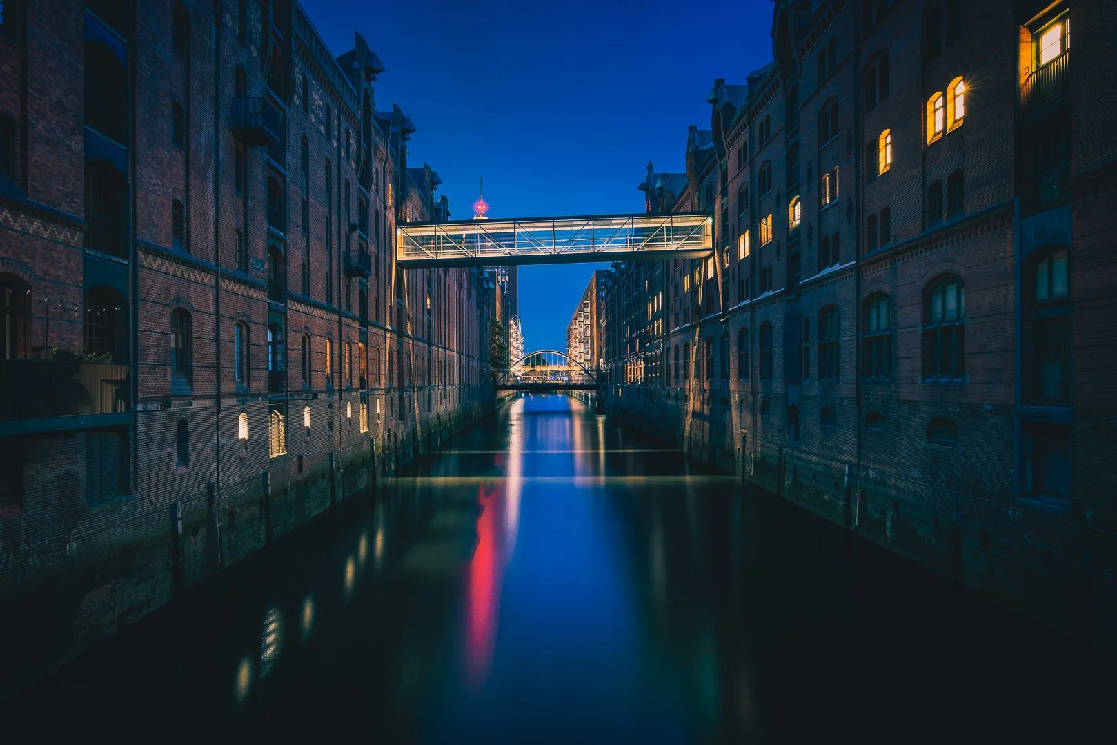 Blue-hour view of Hamburg’s Speicherstadt with historic brick warehouses, a footbridge and red reflections in the canal.
