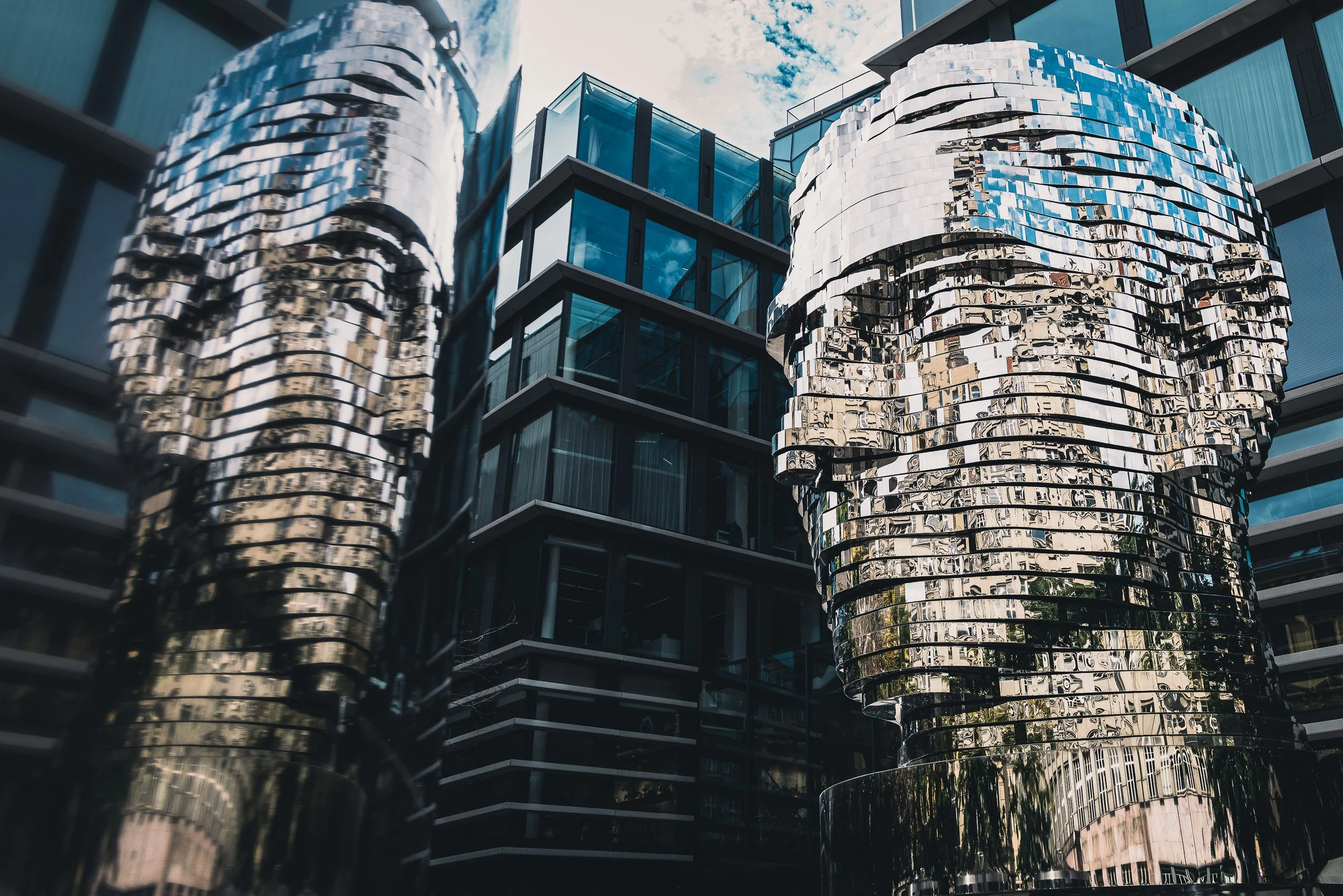 Mirrored metal head sculpture beside modern buildings in Prague