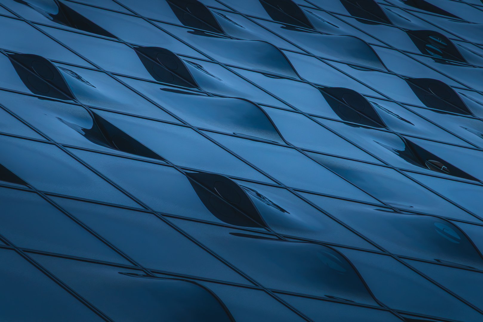 Abstract close-up of the Elbphilharmonie facade in Hamburg with repeating dark curved windows forming a rhythmic pattern.
