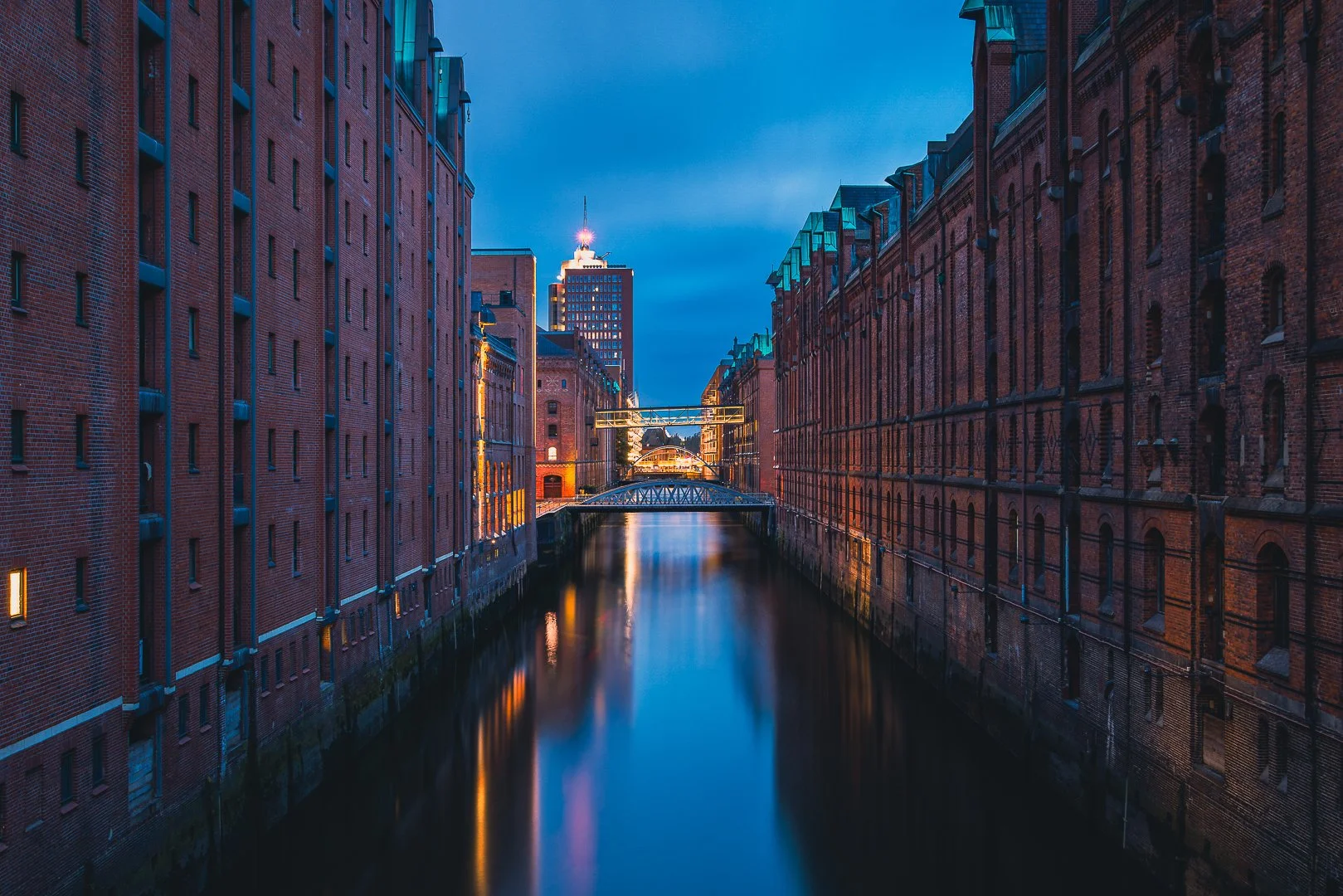 Evening view along a canal in Hamburg’s Speicherstadt with illuminated brick facades reflected in the water.