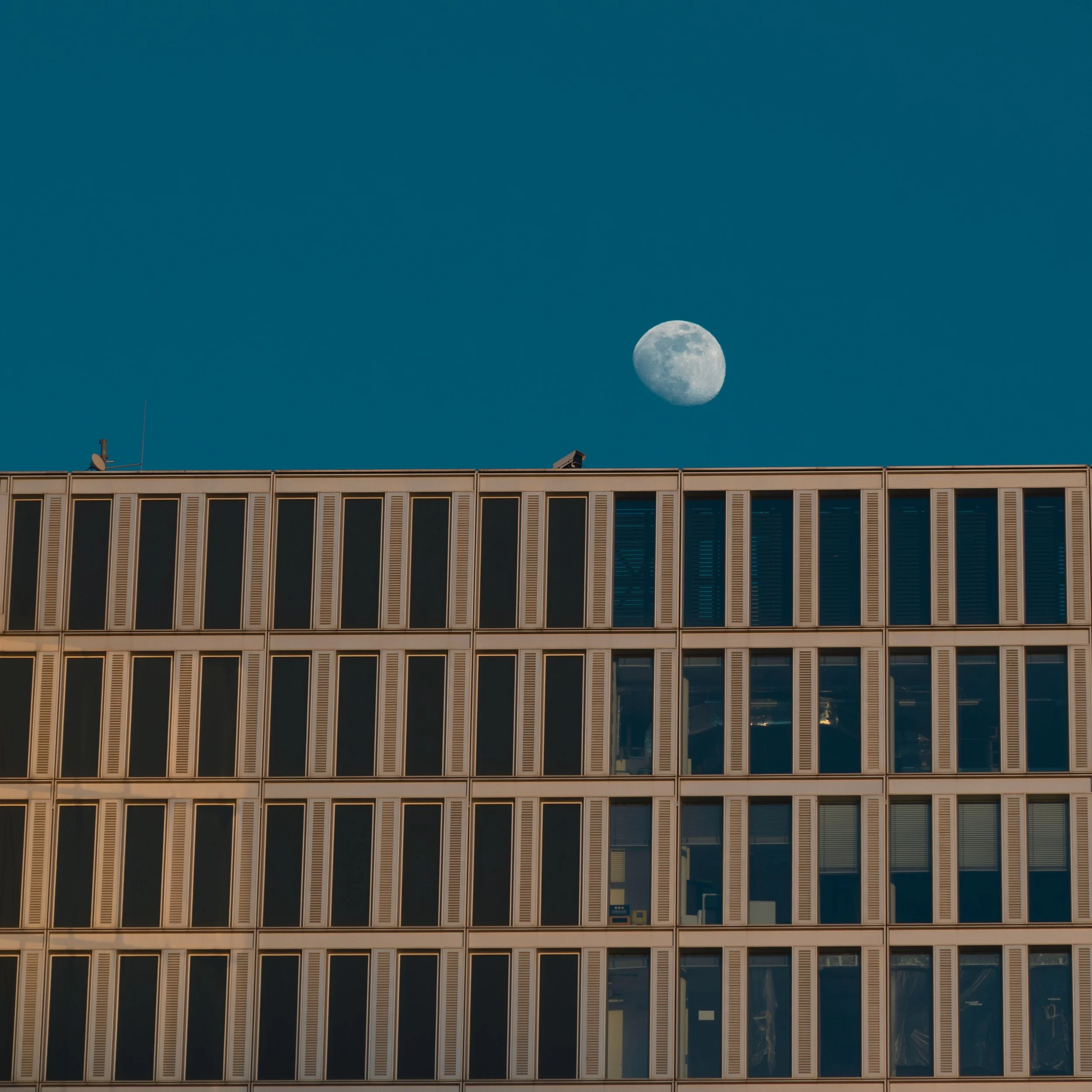 Moon rising above the geometric roofline of a modern building in Frankfurt