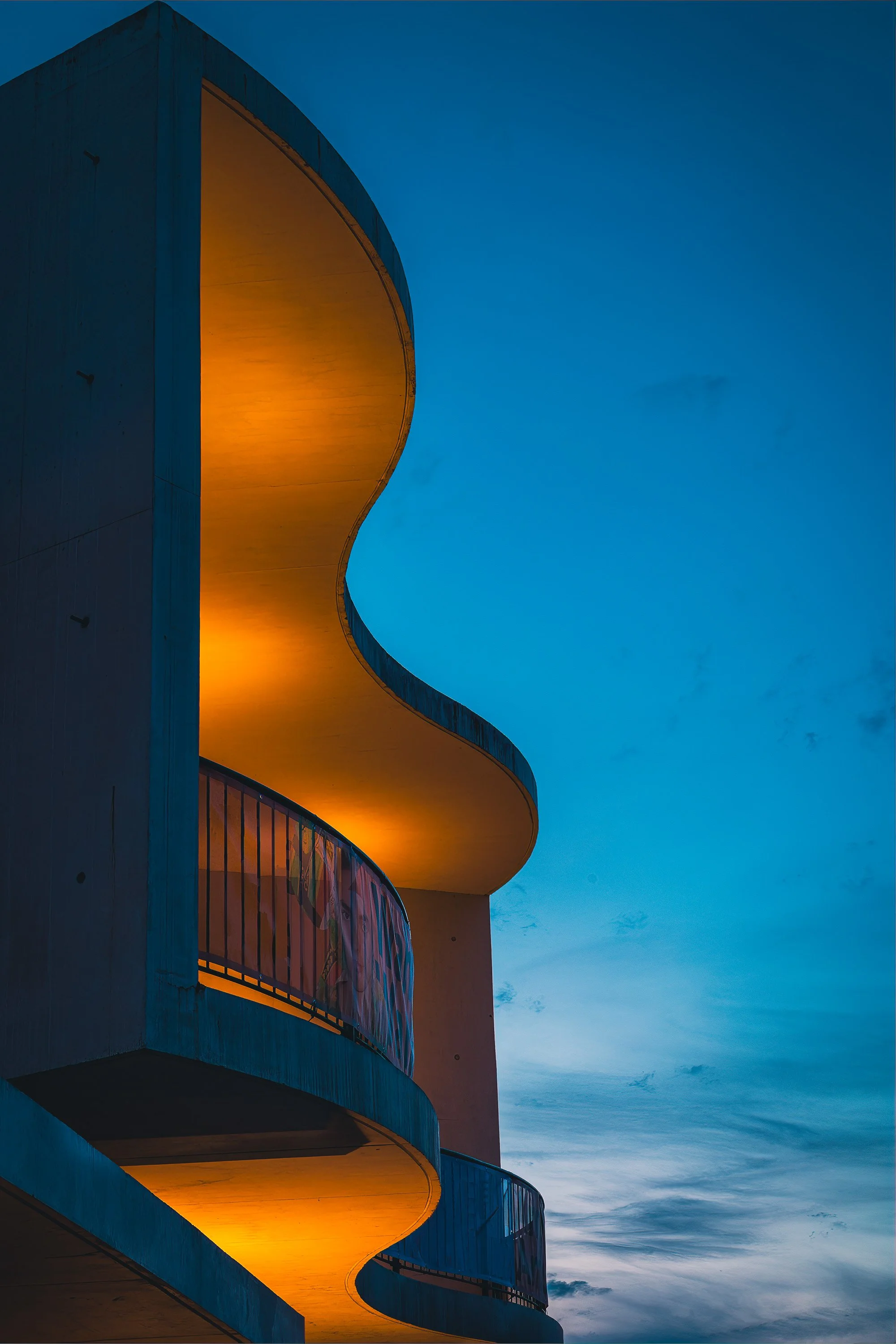 Curved concrete balconies illuminated by warm light against a deep blue evening sky