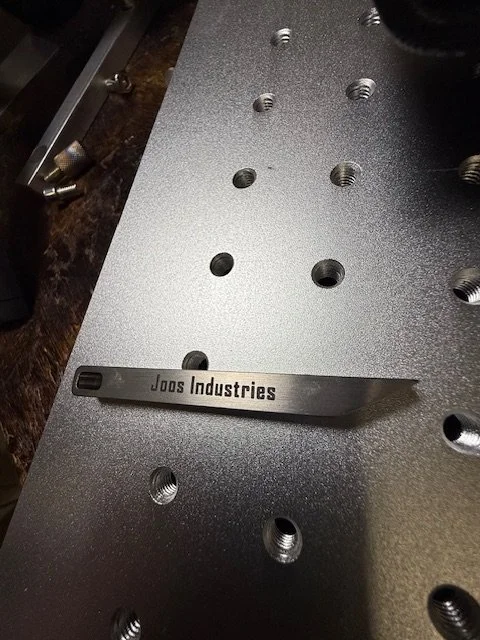 Close-up of a metallic surface with multiple threaded holes, a small black metal tool with the label 'JOBS Industries' resting on it.