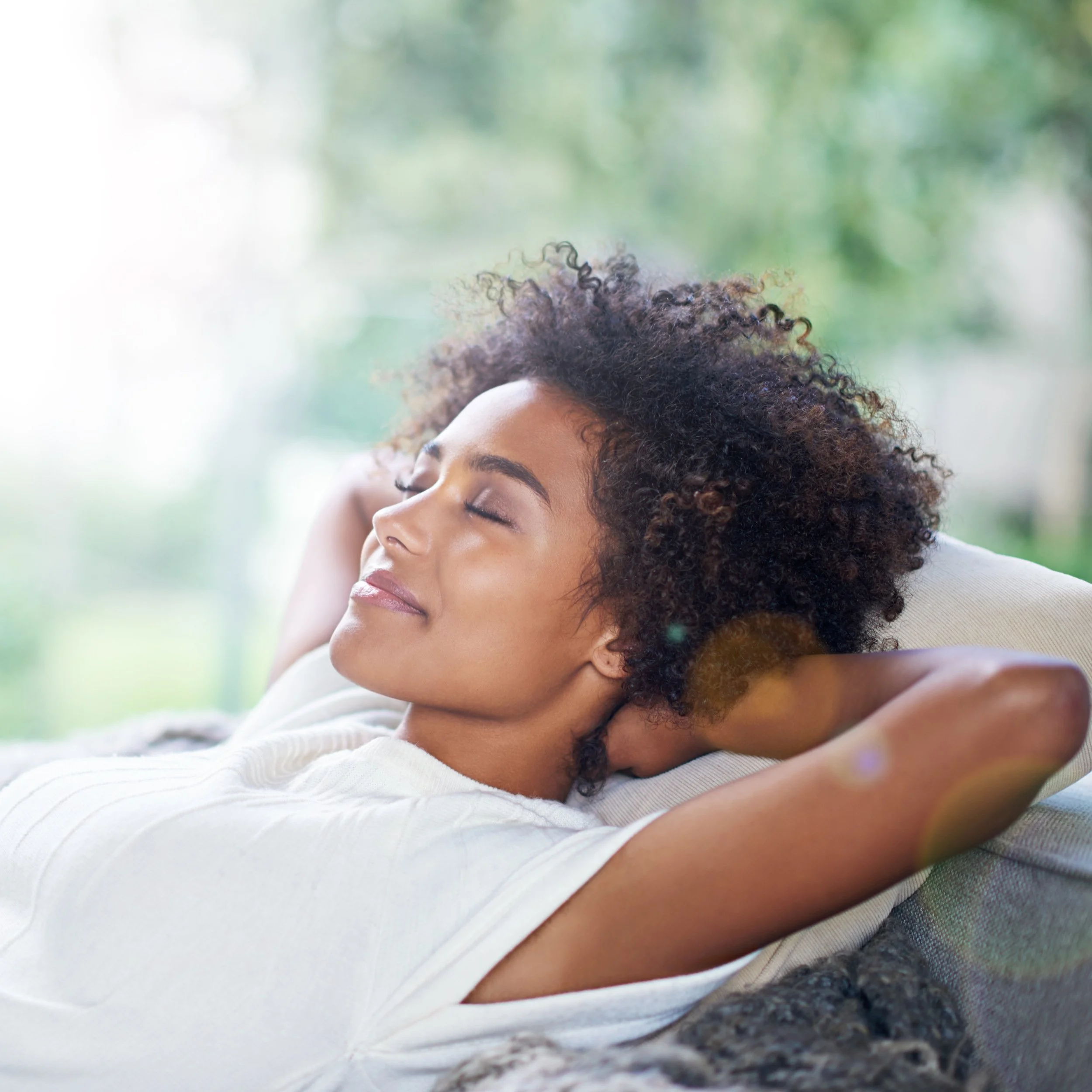 A woman with curly hair relaxing with eyes closed on a couch outdoors