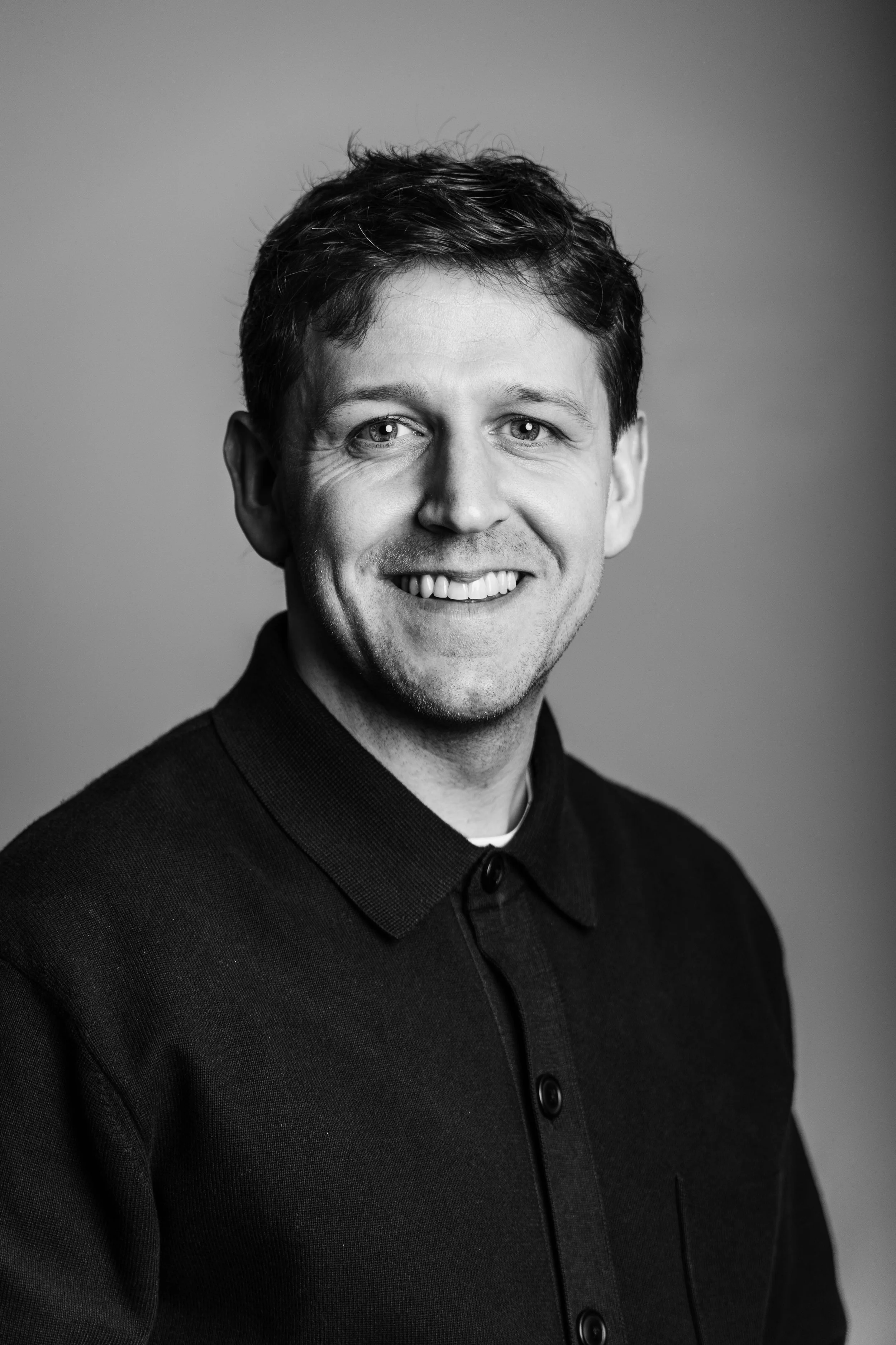 Black and white portrait of a smiling man wearing a dark button-up shirt.