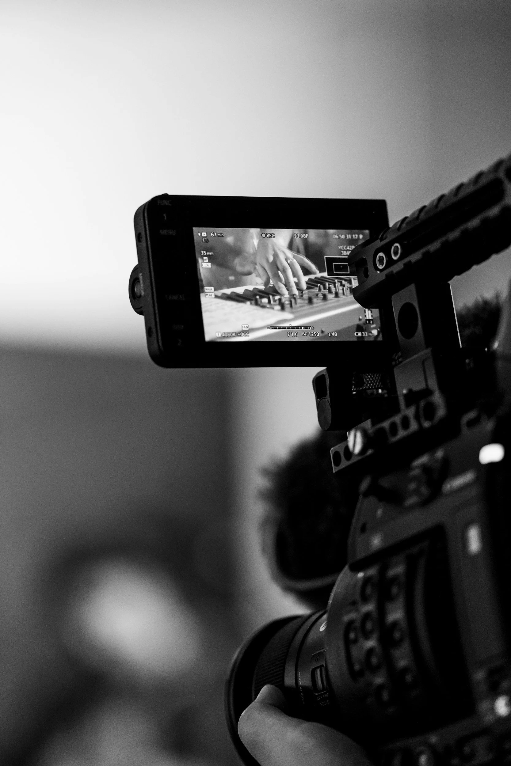 A camera filming a person playing a keyboard, shown on the camera screen in black and white.