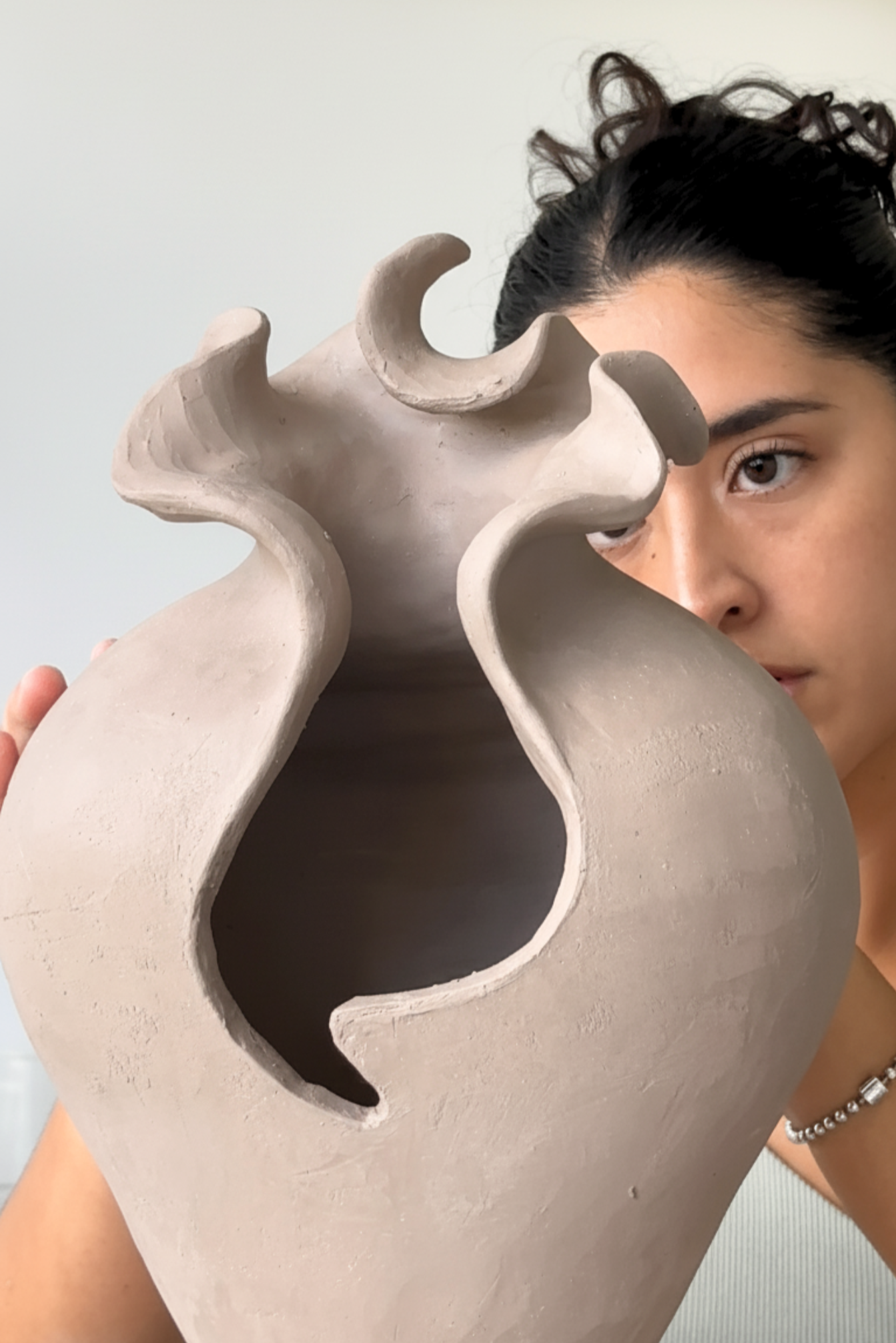 Person holding a large, abstract ceramic sculpture with curved openings.