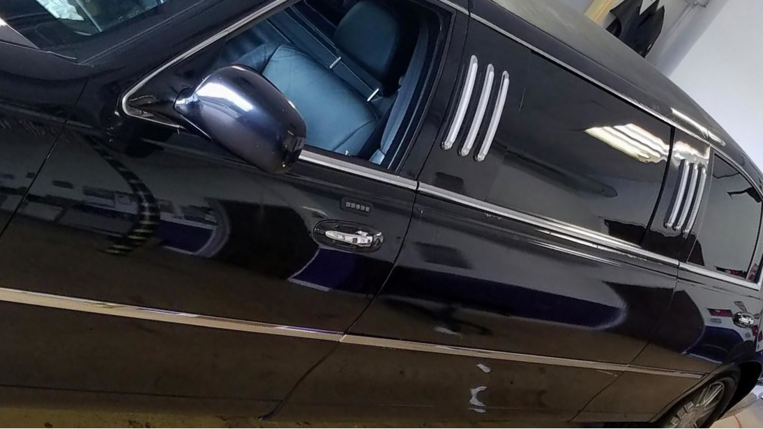 Side view of a sleek black luxury car parked indoors, with reflections of fluorescent lights on its surface.