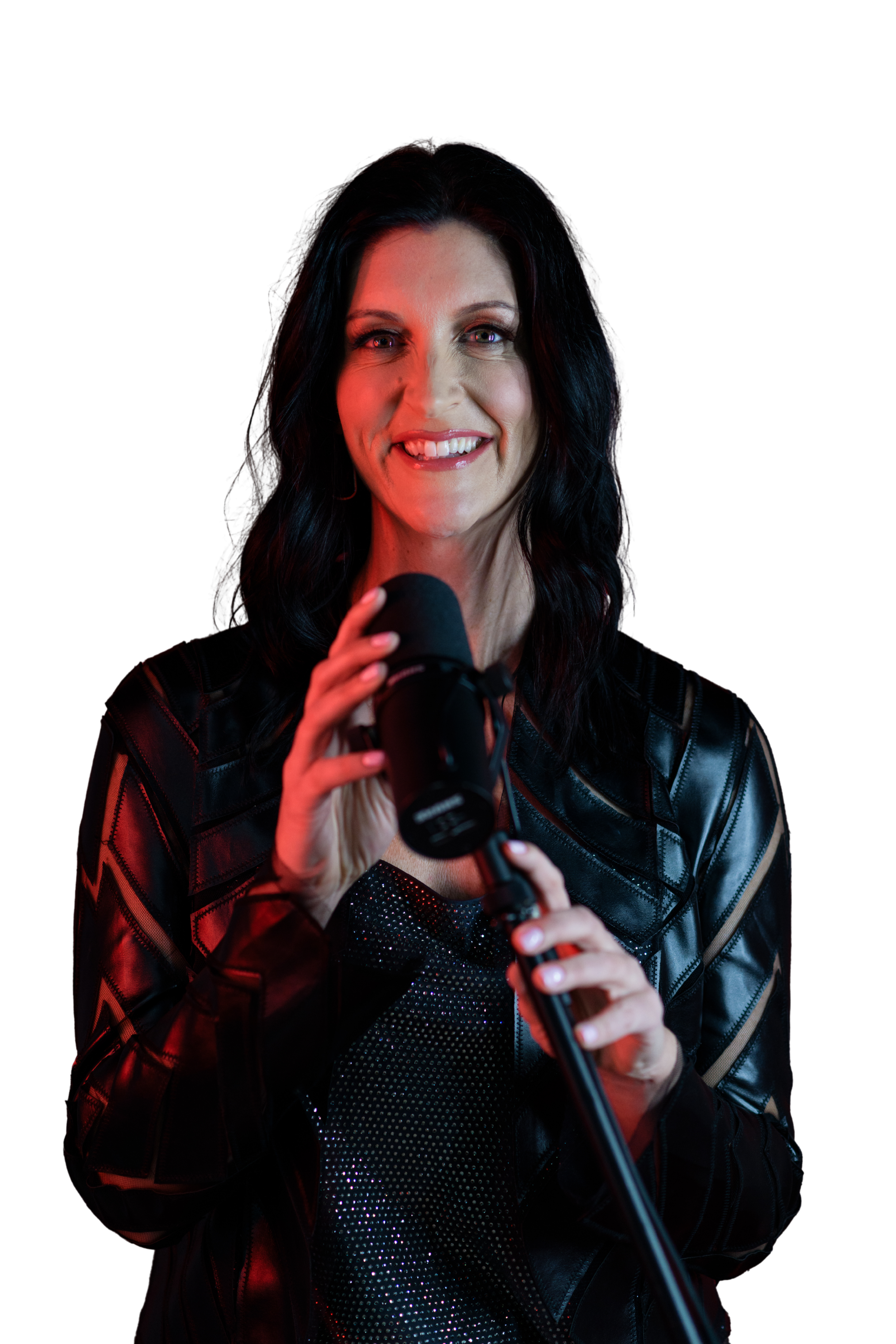 A woman with dark hair and light skin smiling while holding a microphone, dressed in a black leather jacket, against a black background.