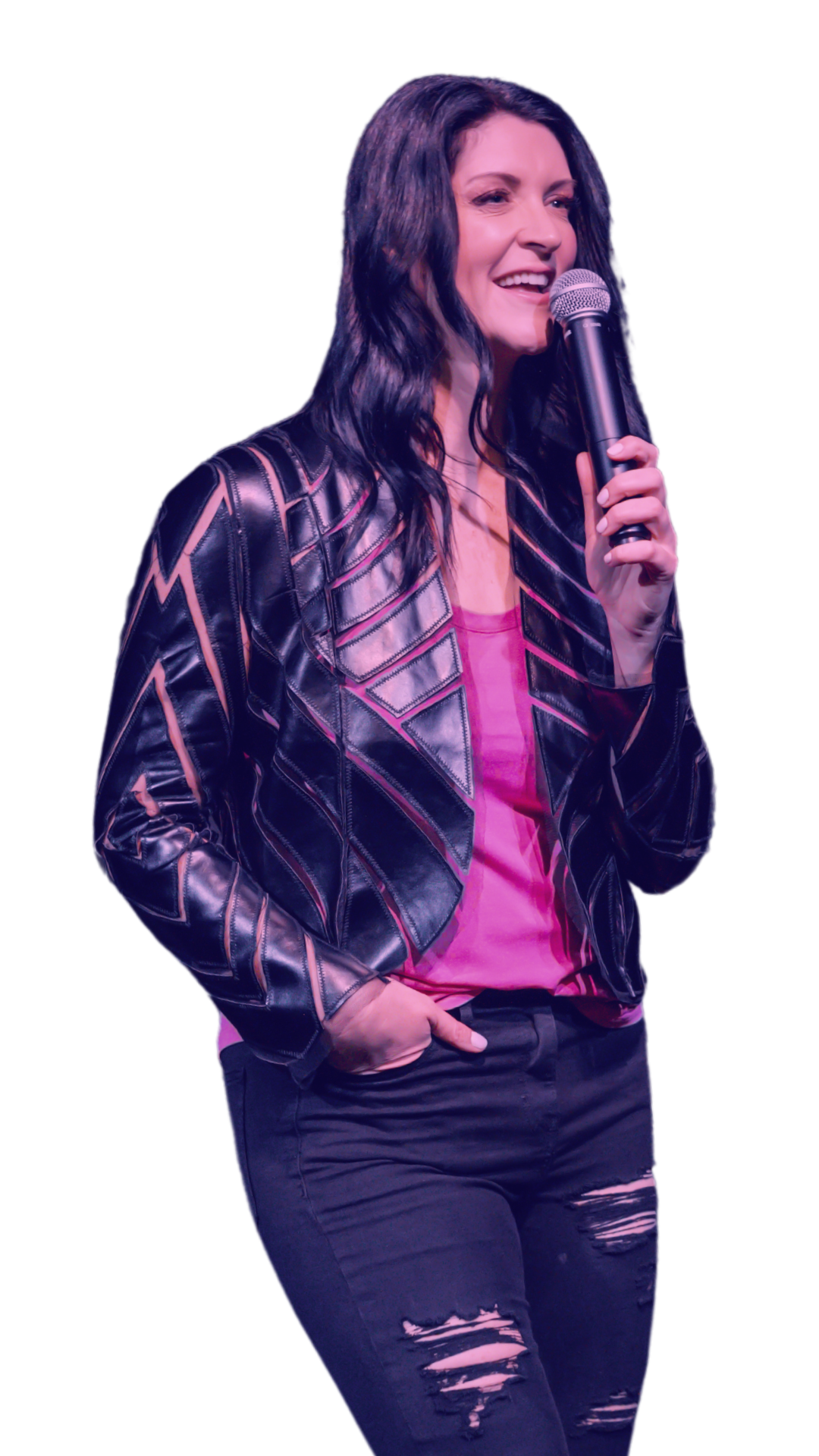A woman with long black hair, wearing a black leather jacket with geometric pink and black patterns, a pink top, and ripped black jeans, holding a microphone and smiling.