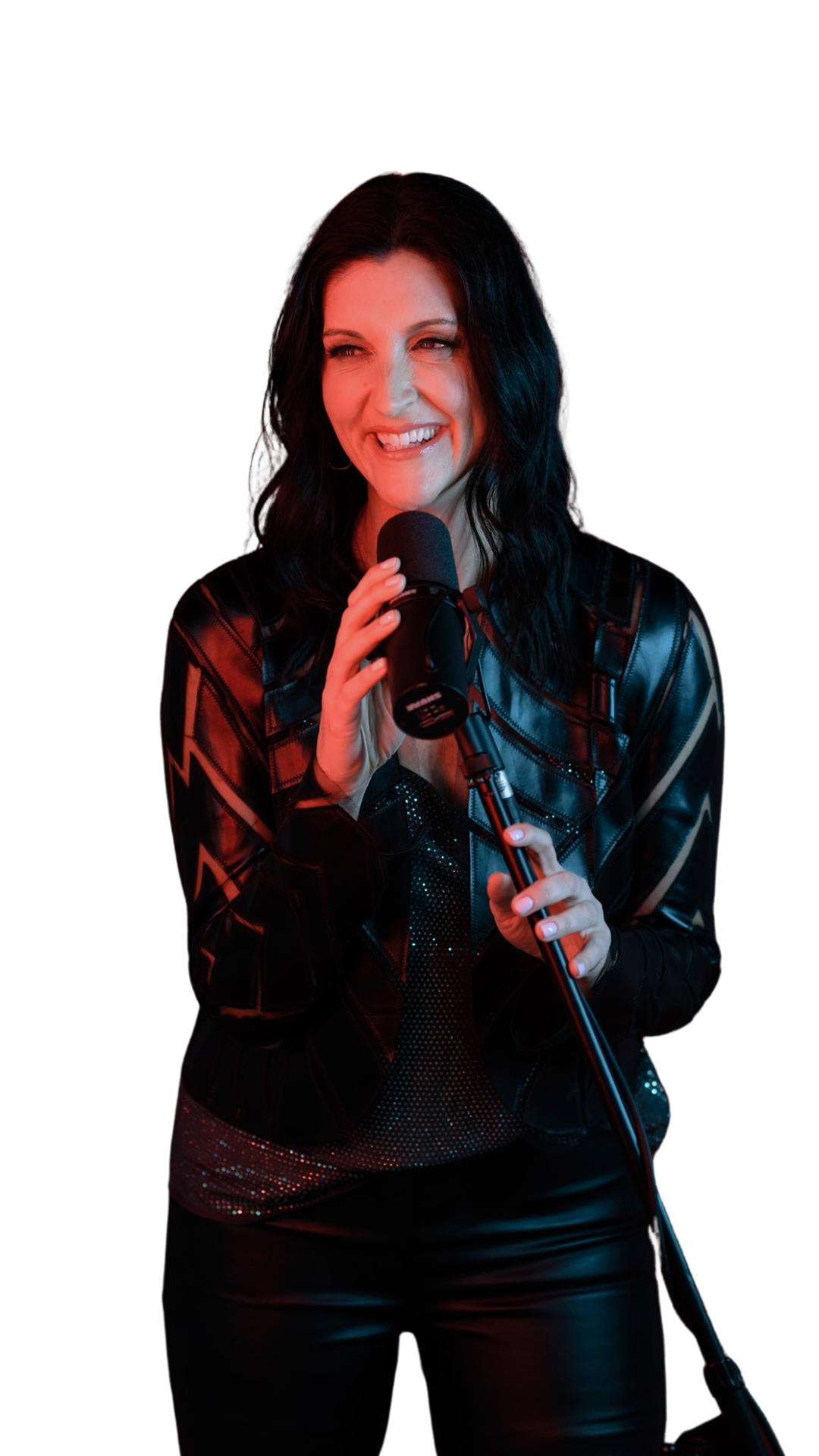Woman with black hair smiling and holding a microphone, dressed in a shiny black leather jacket and black shiny skirt, against a black background.