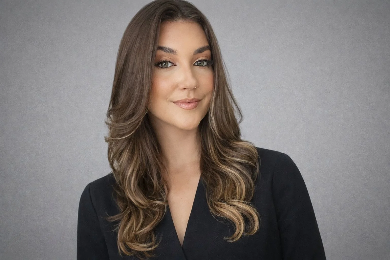 Retrato de uma mulher com cabelo castanho claro, olhos claros, pele clara e vestindo blusa preta, sorrindo suavemente, em fundo cinza