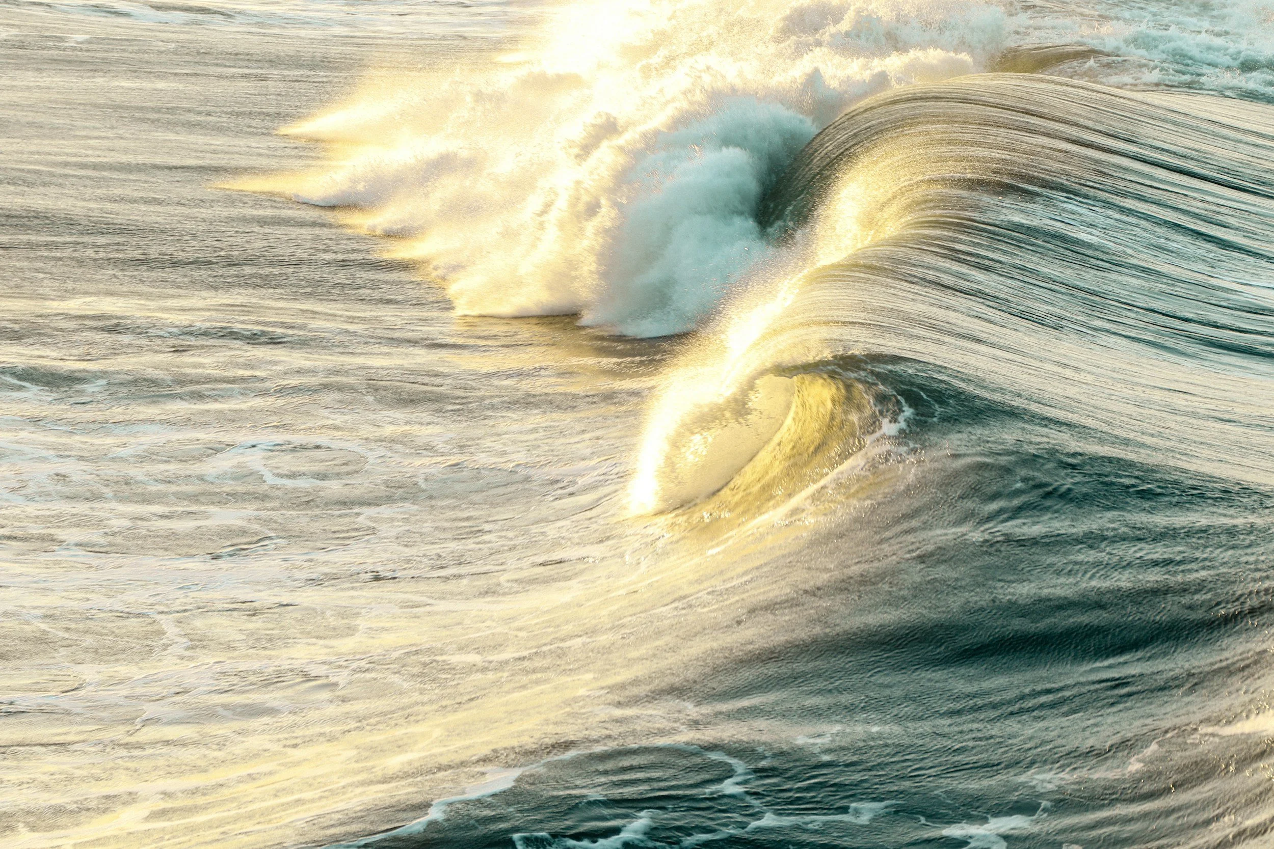 Waves crashing in the ocean during sunset with golden sunlight reflecting off the water
