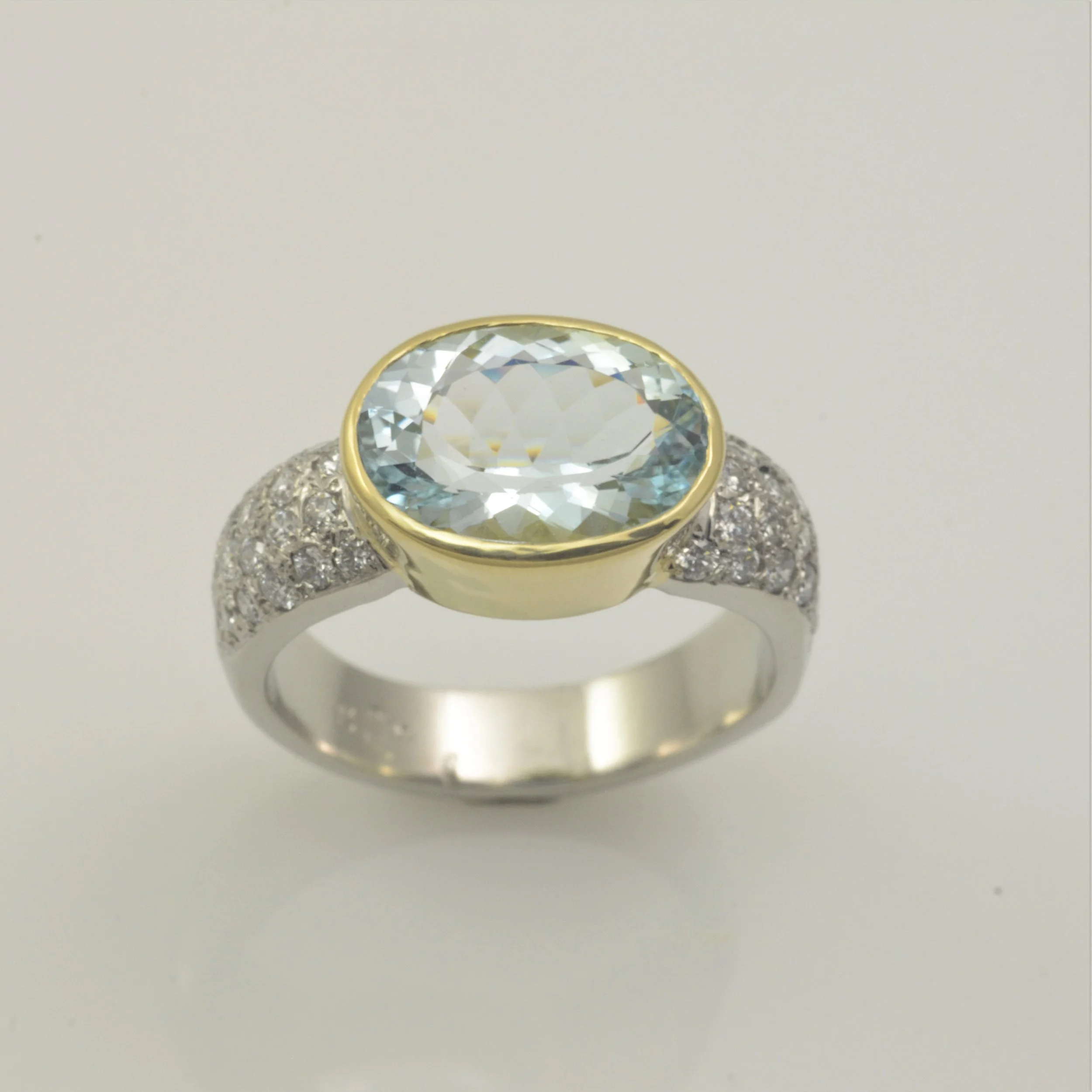 A ring with a large oval-cut aquamarine blue gemstone in a gold setting, flanked by small diamonds on a white gold band.