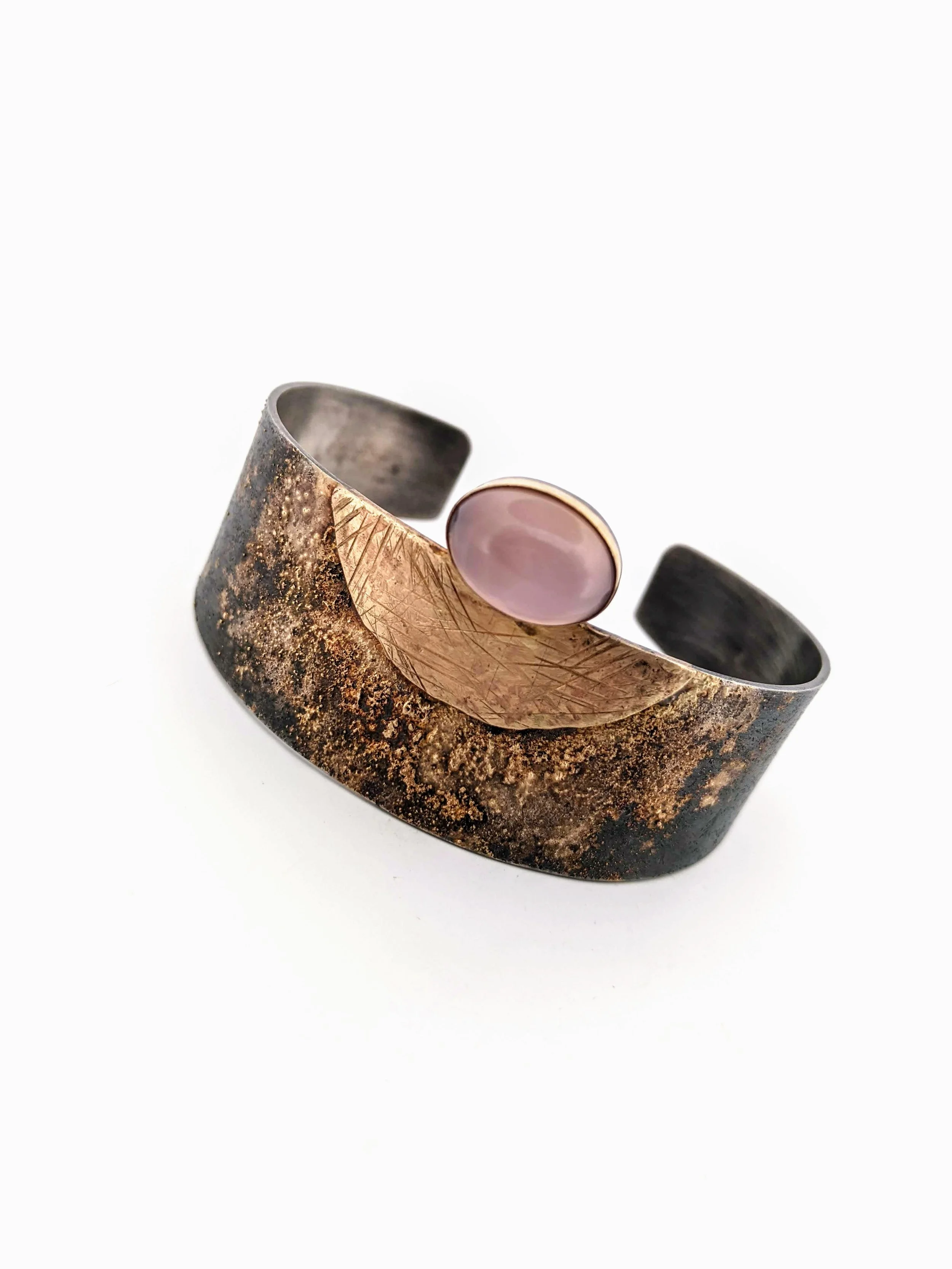 A mixed metal cuff bracelet with gold and silver and a rosé-colored oval chalcedony gemstone and engraved gold accents.