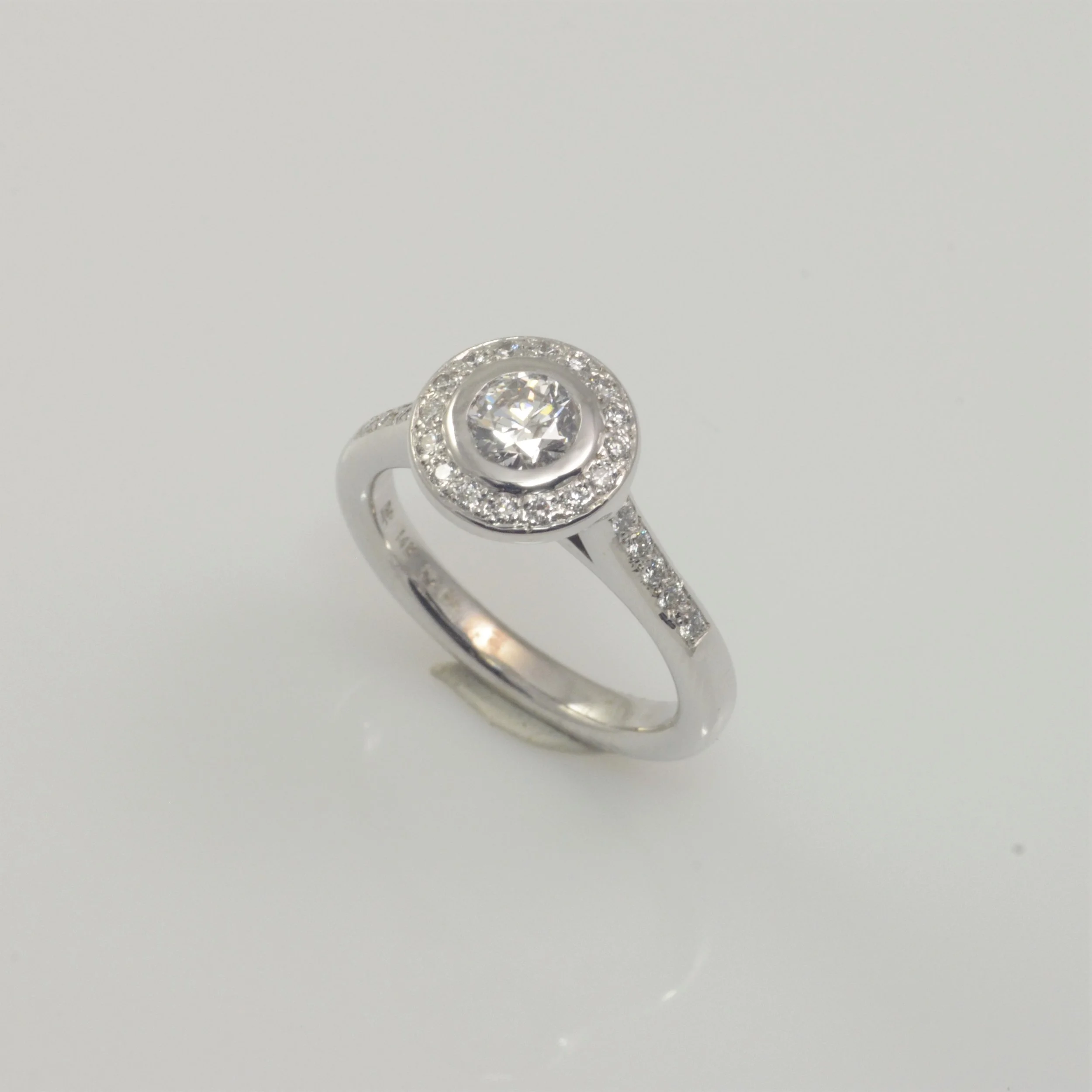 Silver ring with a central diamond surrounded by smaller diamonds, set on a plain white background. Perfect for an engagement.