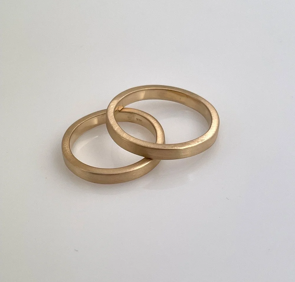 Two gold wedding bands on a white surface.