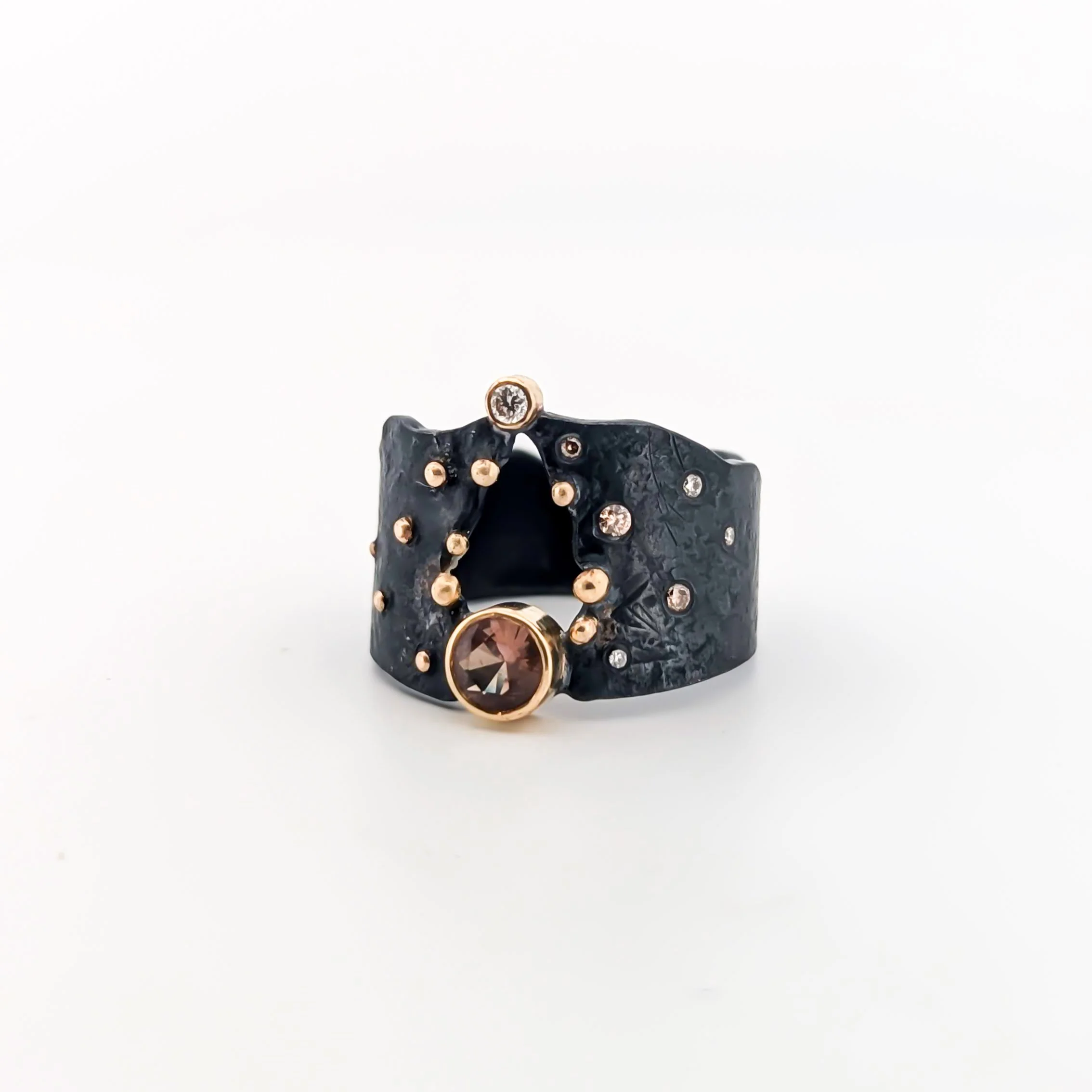 Black oxidized sterling silver textured wide ring with gold accents and orange sapphire and diamonds, featuring a large gemstone on the front and smaller gemstones around the band. Design by Rocky Pardo Jewelry.