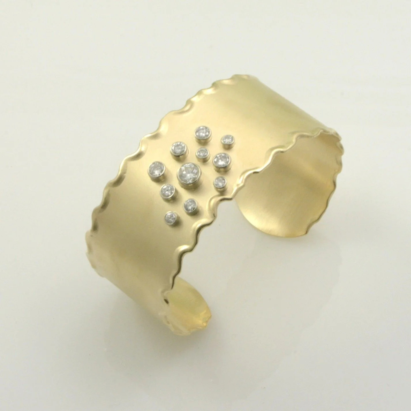 A gold cuff bracelet with wavy edges decorated with small diamonds. Design by Bill Wismar.