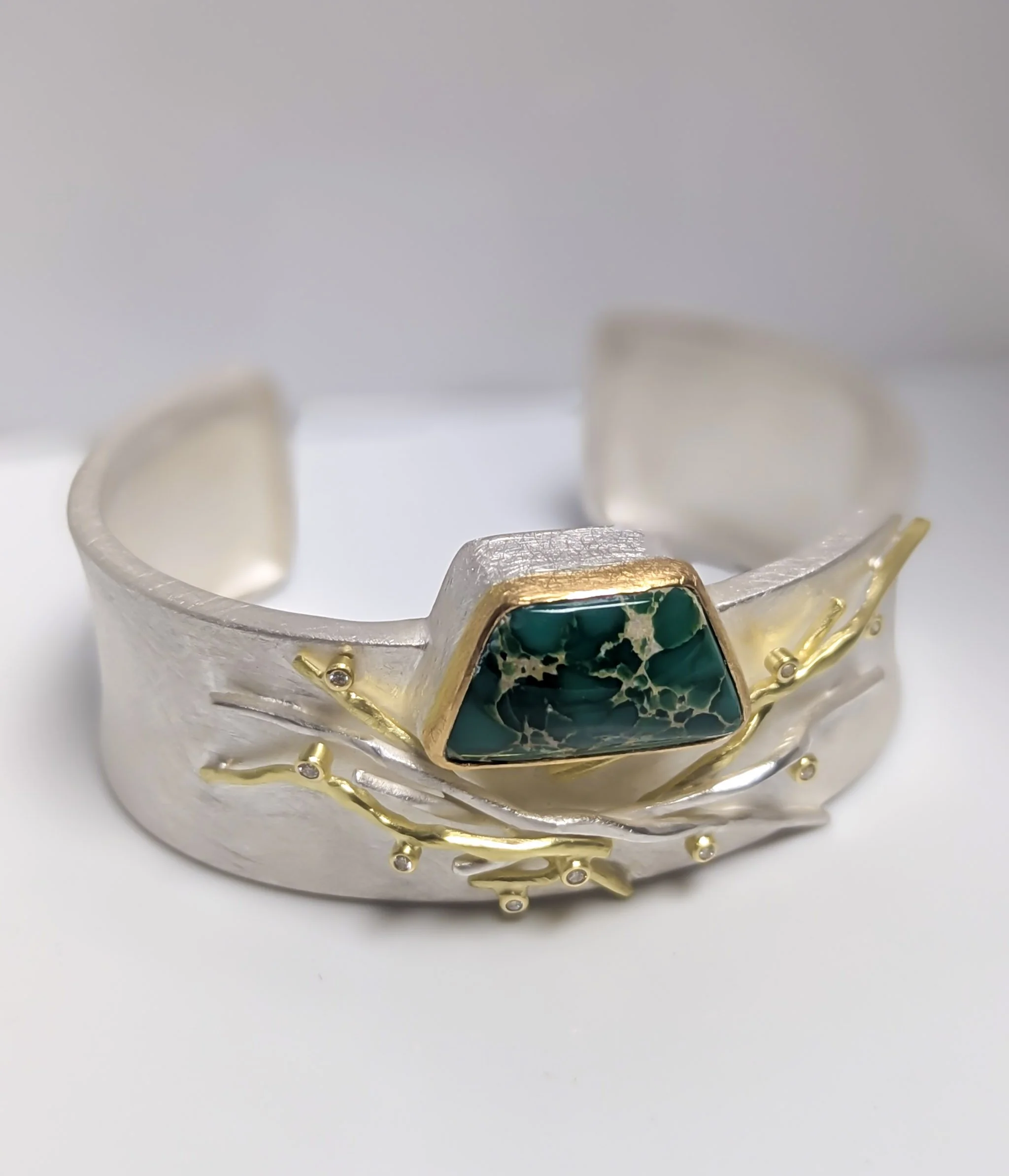 Silver cuff bracelet with a green and black trapezoid variscite stone and gold branch-like accents. Design by Sandra Matasick.
