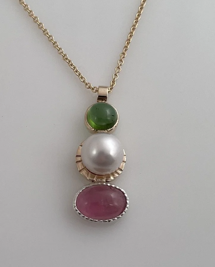 Pendant necklace featuring a green tourmaline stone, a white pearl, and a pink tourmaline stone set in silver and gold. Design by Bill Wismar.