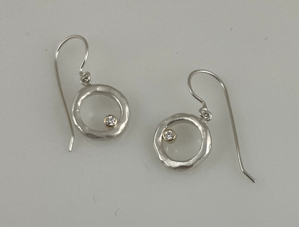 White gold earrings with a circular, textured design and small embedded diamond gemstones, laid on a light surface.
