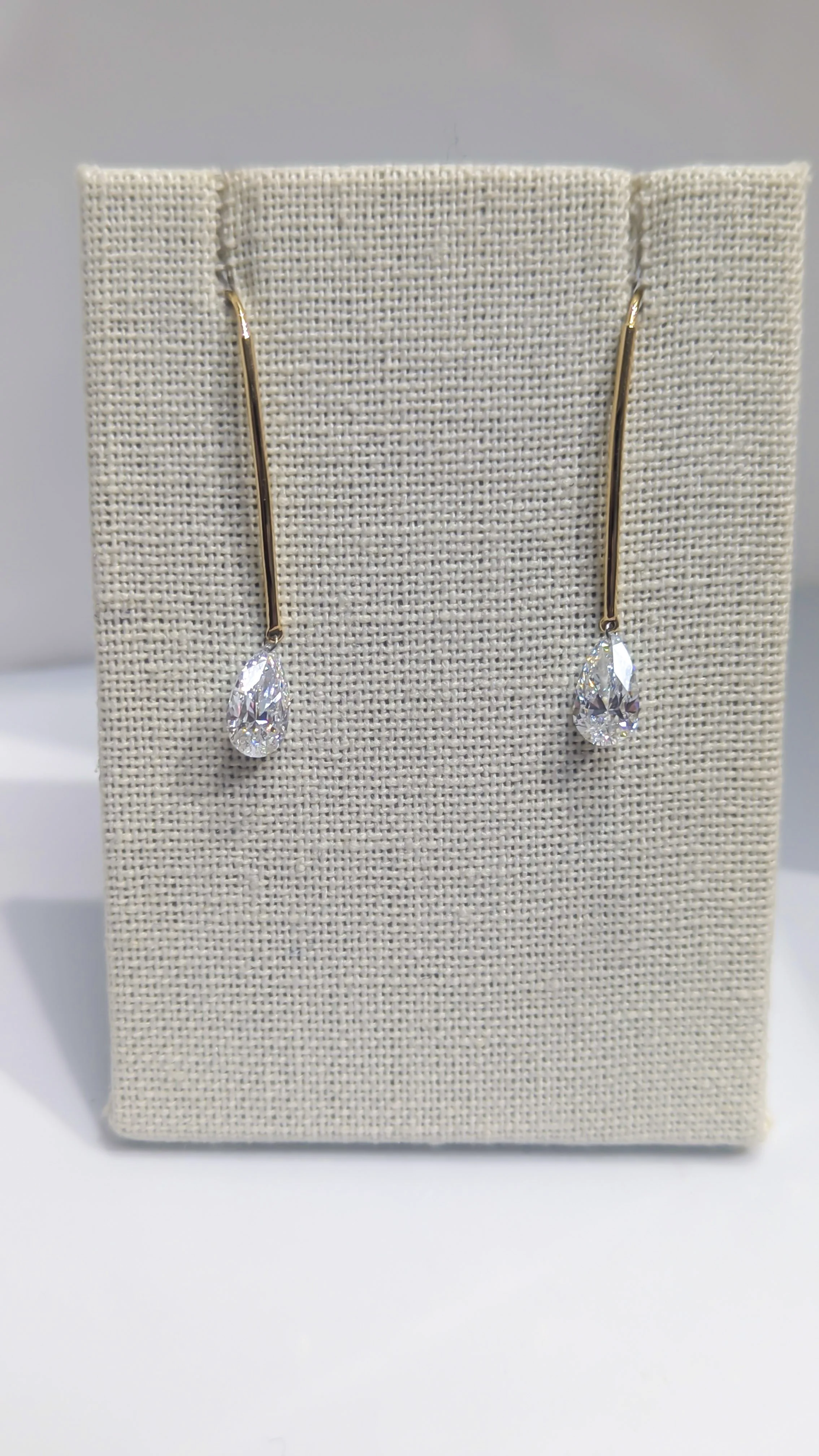 Gold drop earrings with teardrop-shaped diamonds, displayed on a beige fabric jewelry card.