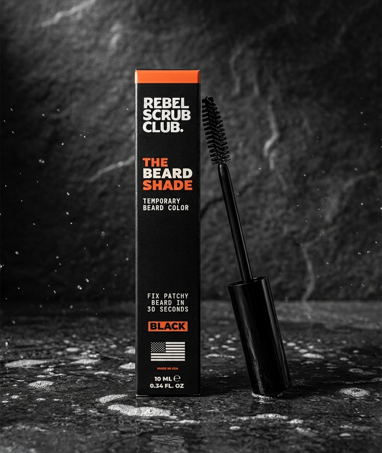 A black box of Rebel Scrub Club beard color with orange and white text, next to a black mascara-like brush applicator on a dark textured surface.
