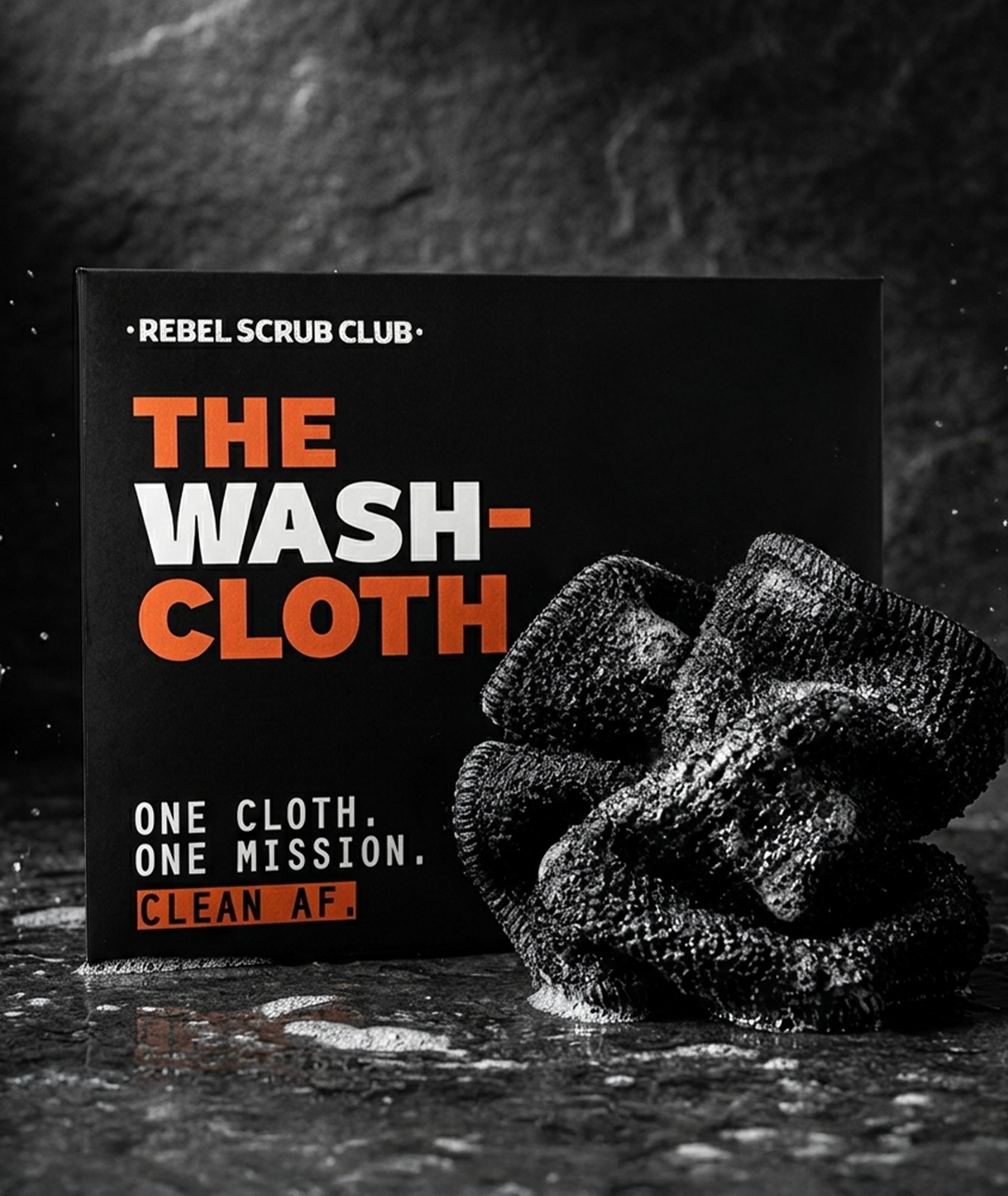 A black box with the text 'Rebel Scrub Club' and 'The Wash Cloth' in orange and white letters, positioned next to a pile of used washcloths on a dark, textured surface.