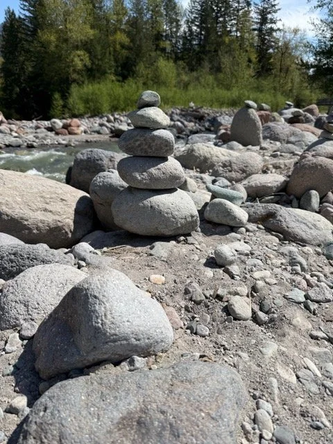 Stacked rocks beside a river with a forest in the background.