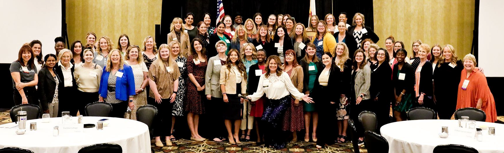 Group picture of the women in leadership members lined up in front of a stage at an event.