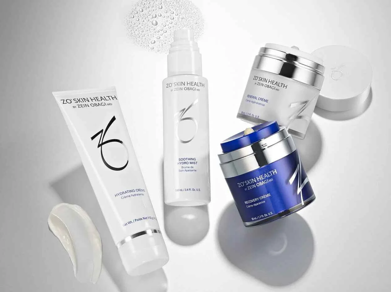 Collection of skincare products from ZO Skin Health, including hydrating cream, soothing hydro mist, renewal creme, and recovery creme, arranged on a light surface with shadows.