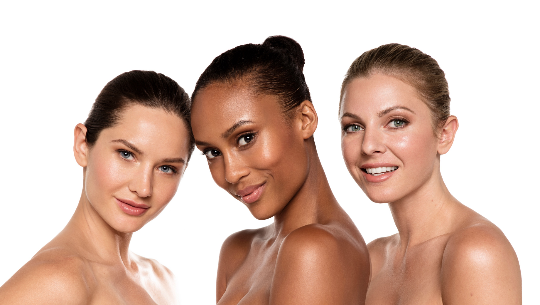 Three women with different skin tones smiling, facing forward, with bare shoulders, against a white background.