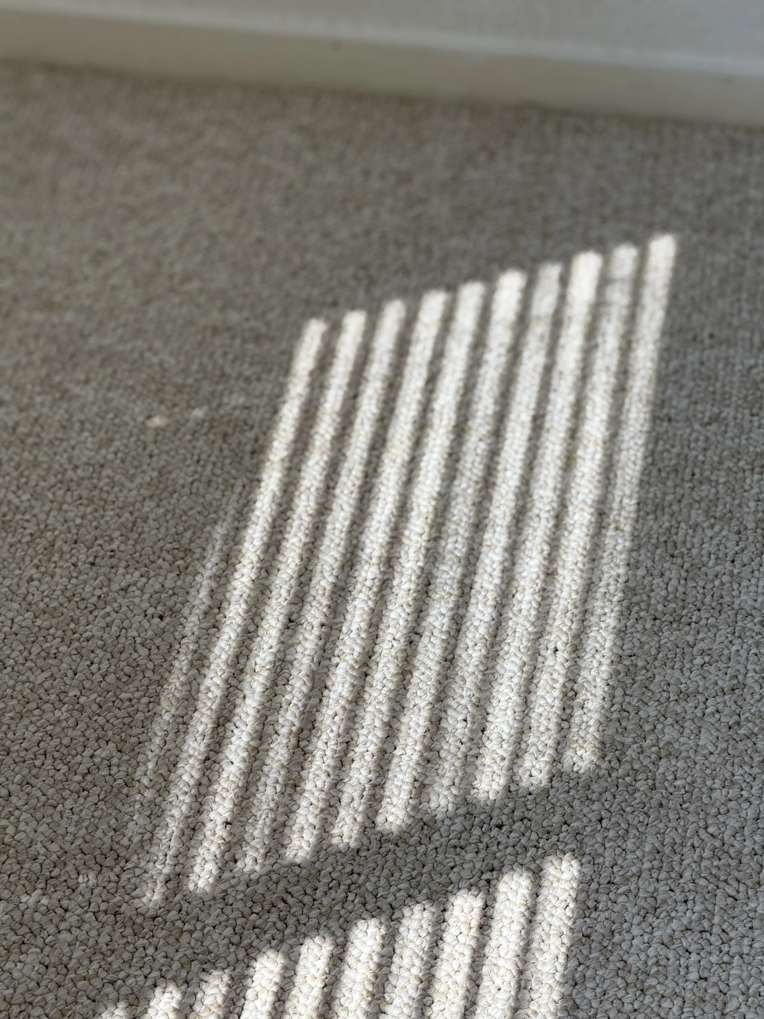 Sunlight passing through window blinds casting striped shadows on a beige carpet.